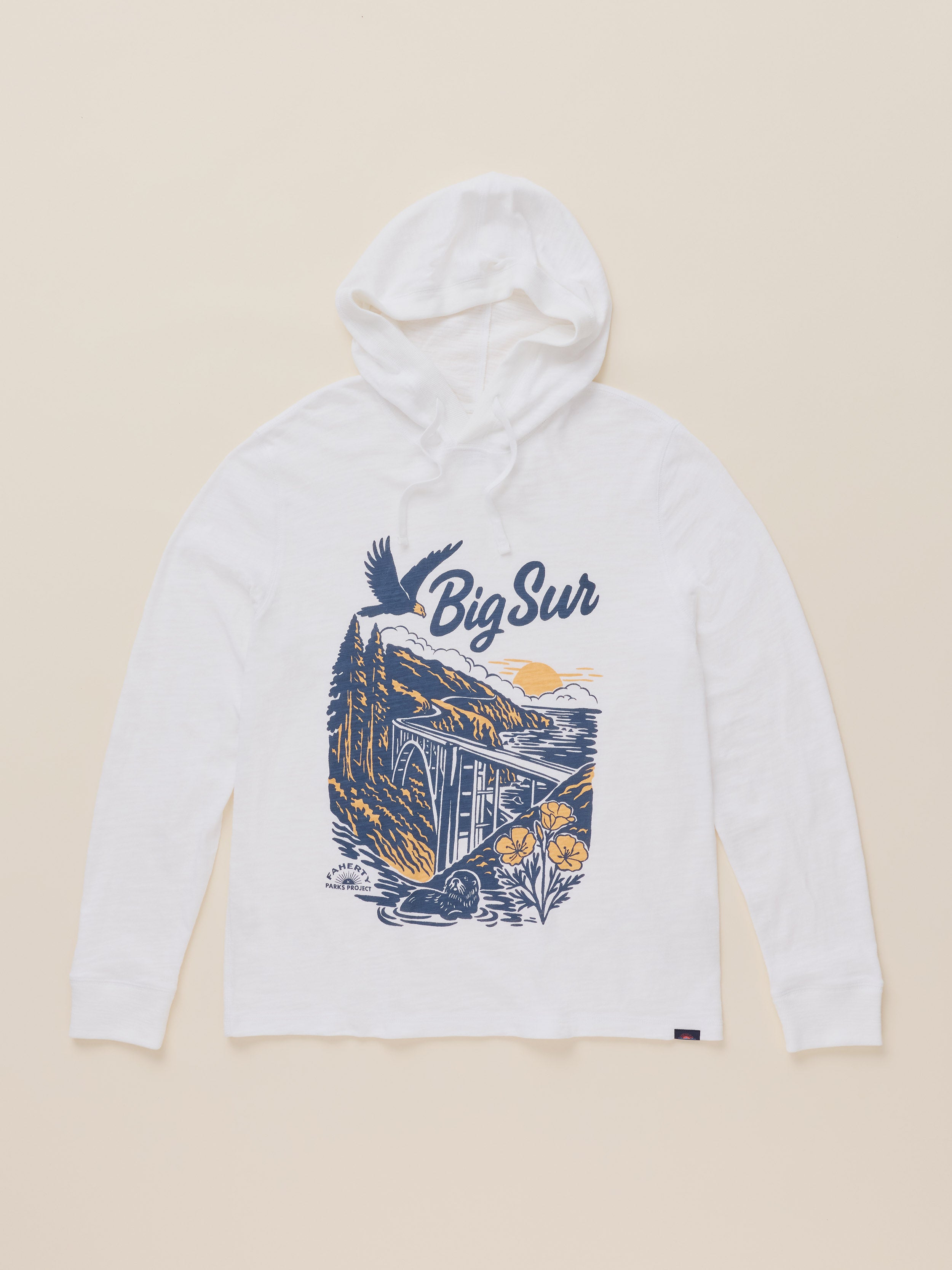A white long-sleeve hoodie with a 'Big Sur' graphic print on the front, featuring a coastal illustration in navy blue, yellow, and orange, laid flat on a light beige background.