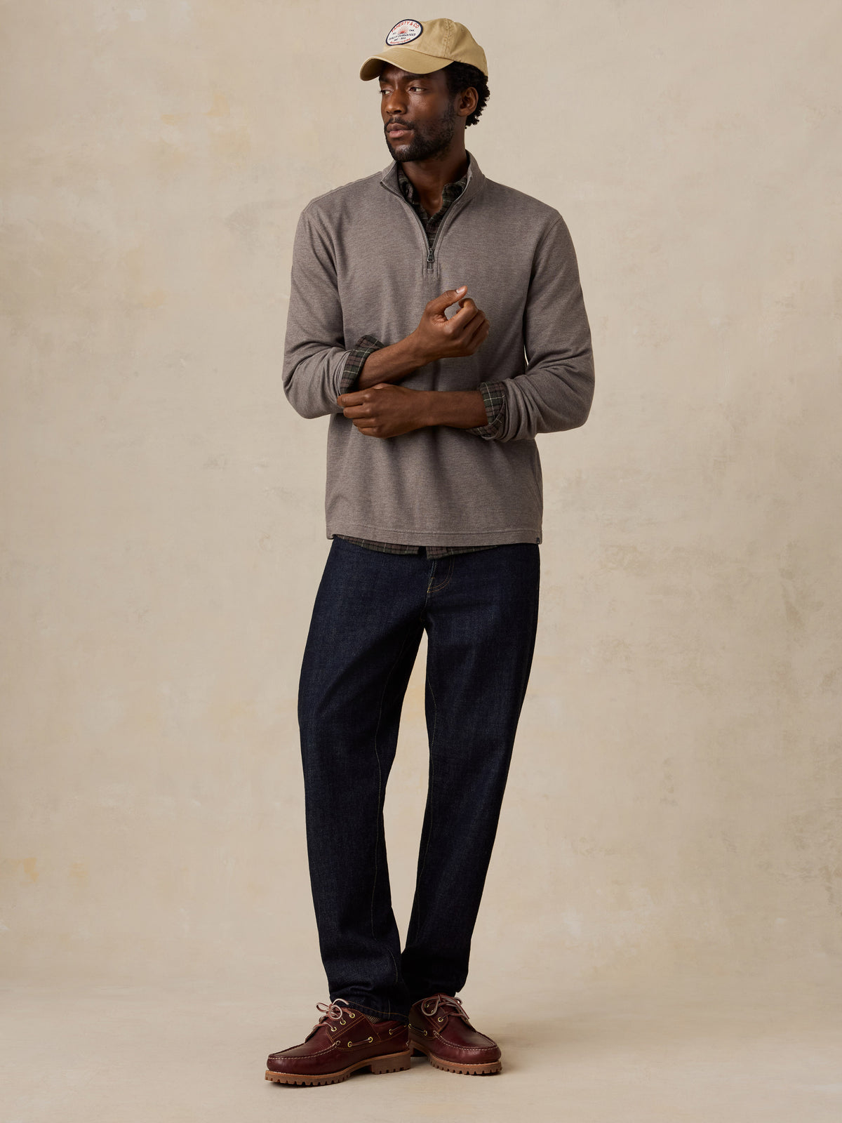 A man wearing a light brown quarter zip and jeans, image 5 of 5