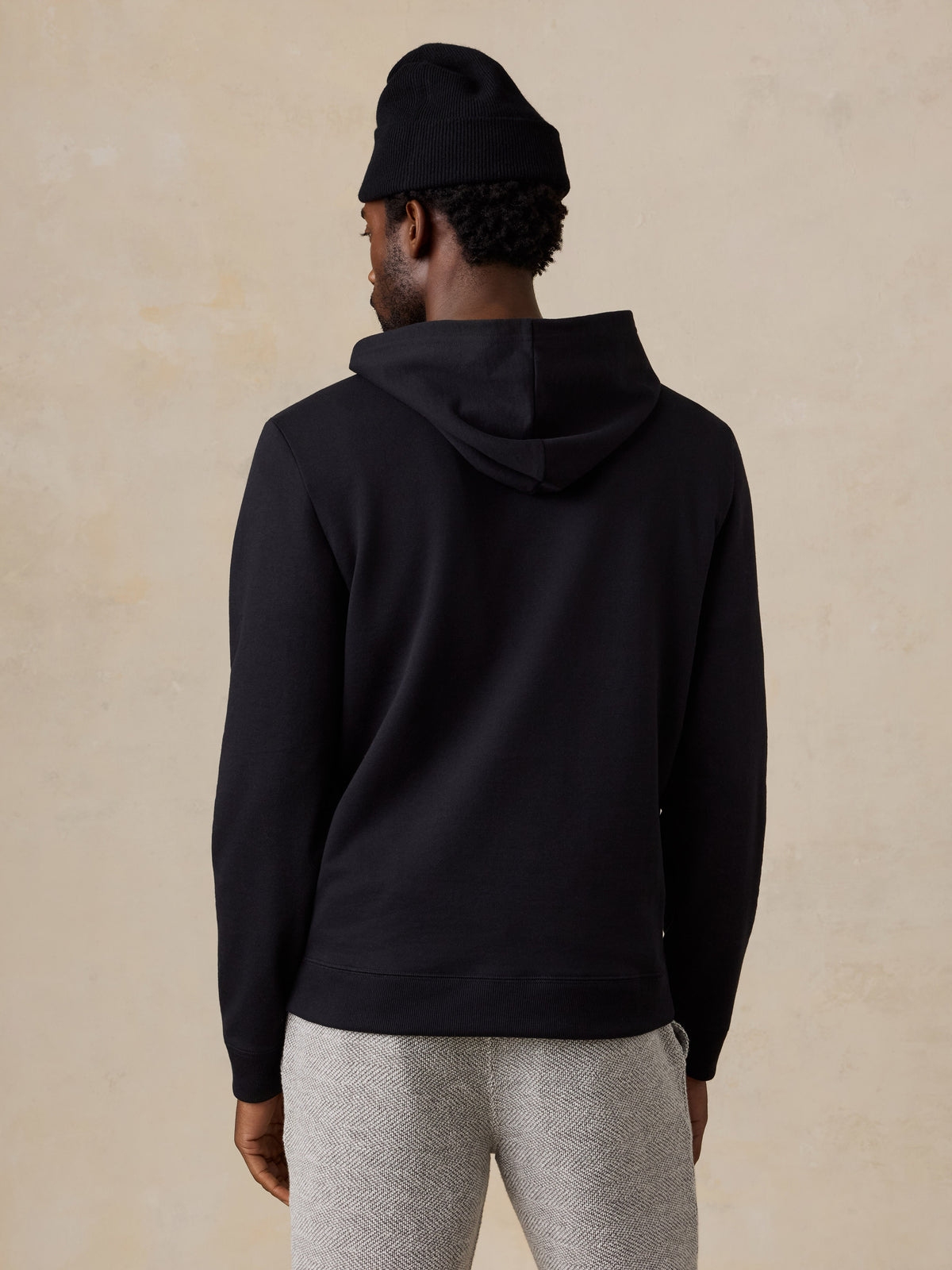 A man viewed from behind wearing a black hoodie and lounge shorts, image 4 of 6