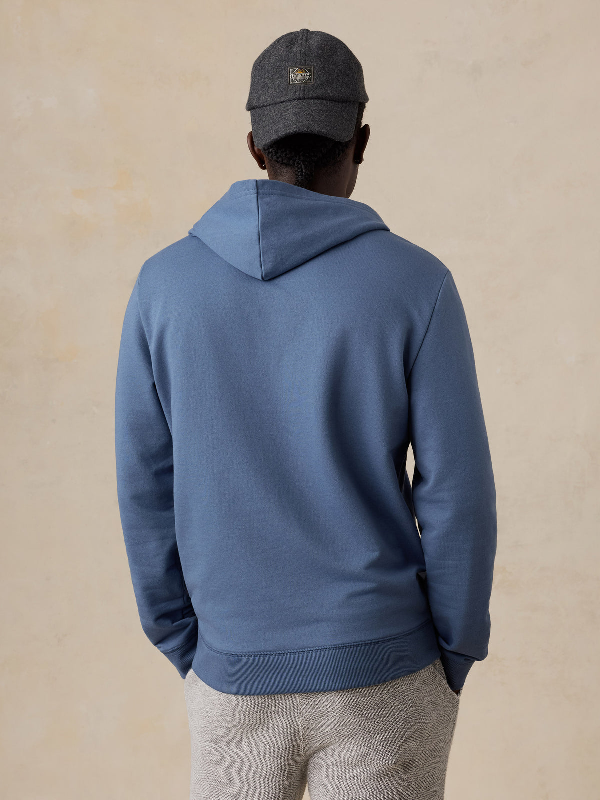 A man viewed from behind wearing a blue hoodie and sweatpants, image 5 of 5