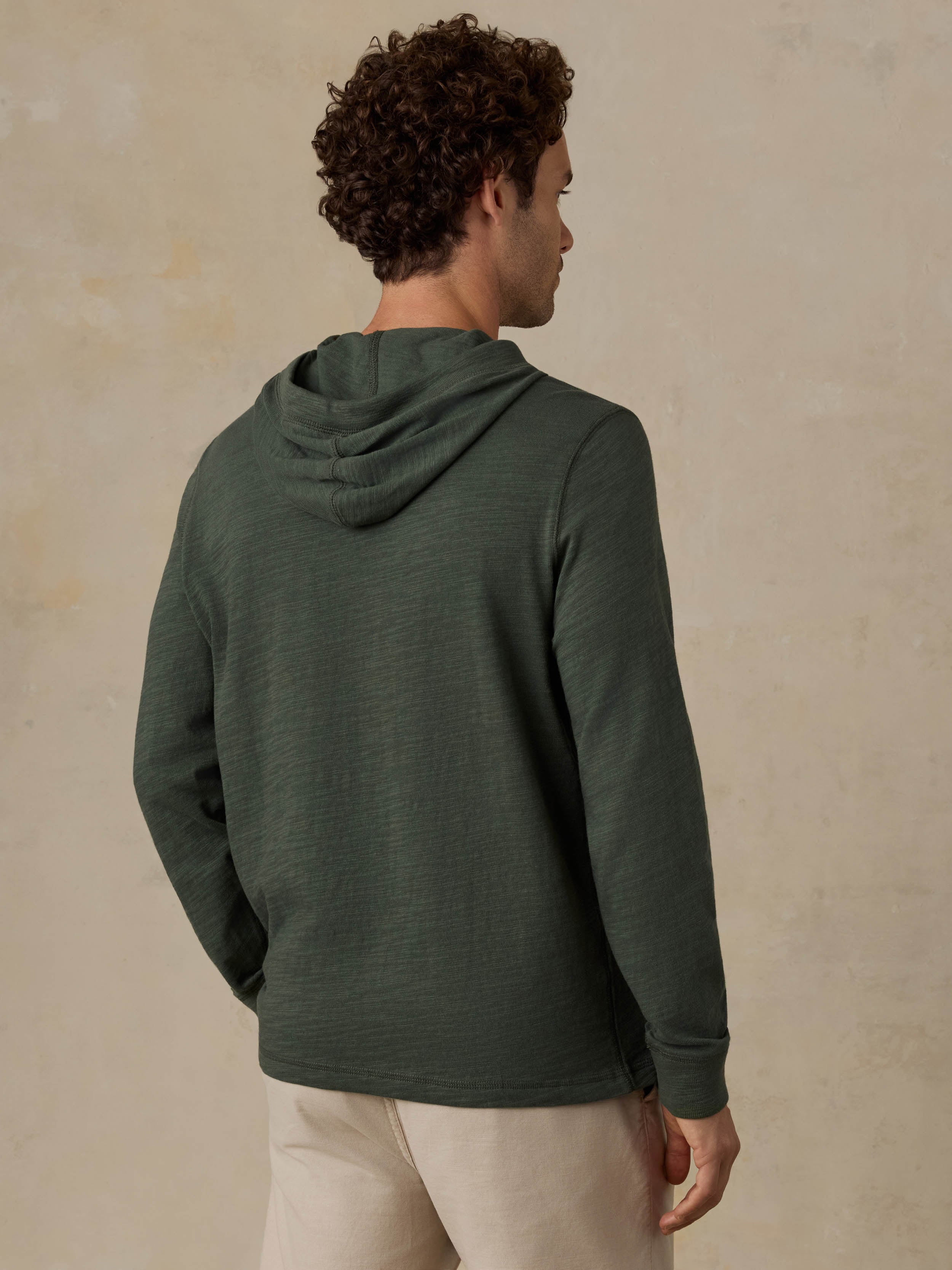 Man wearing a dark olive green hoodie and beige shorts against a beige background