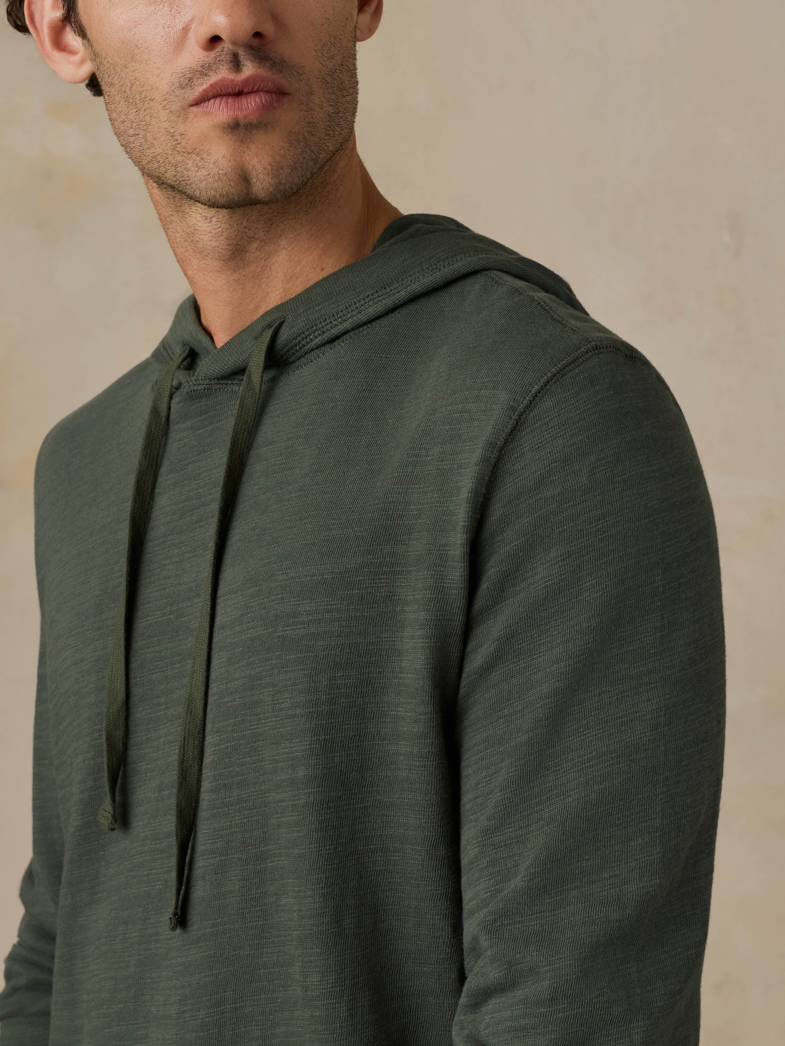 Close-up of a man wearing a dark olive green hoodie against a beige background