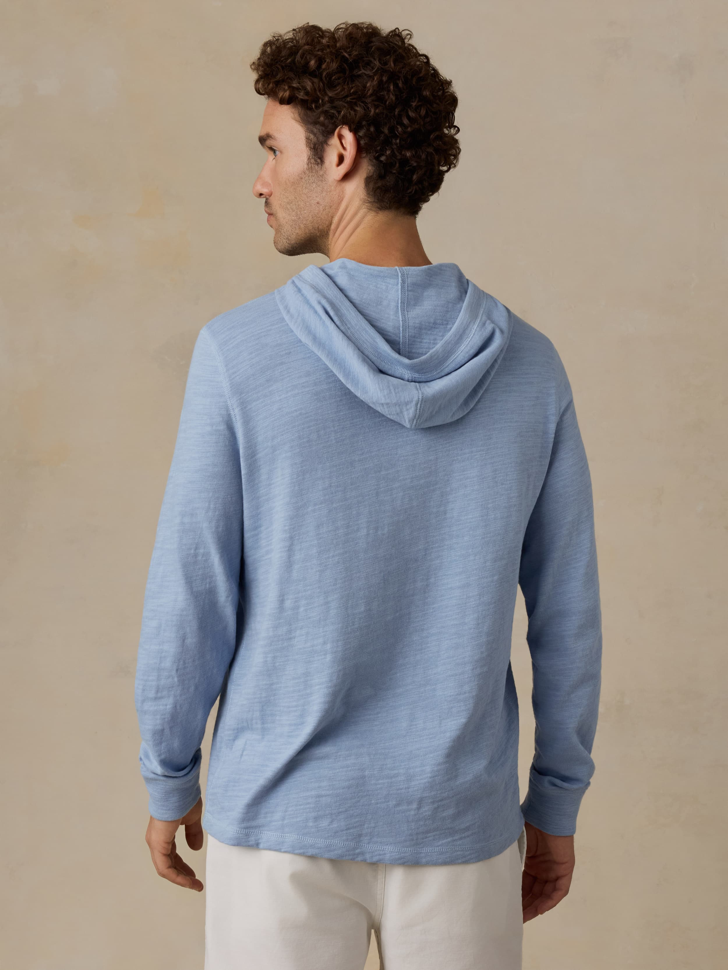 Man wearing a blue hoodie and beige shorts against a beige background