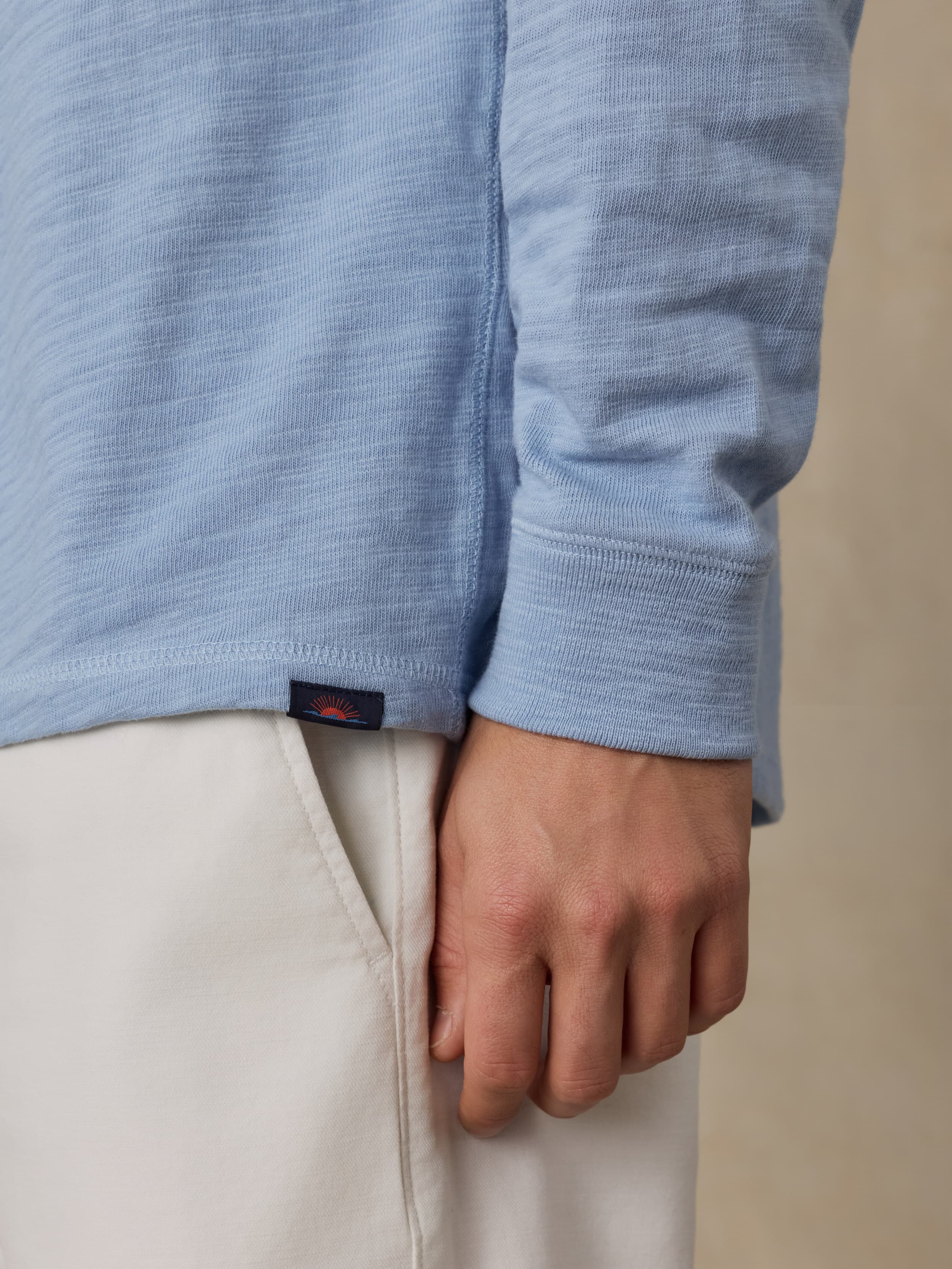 Close-up of a person wearing a light blue sweater with a Faherty brand logo and beige shorts.