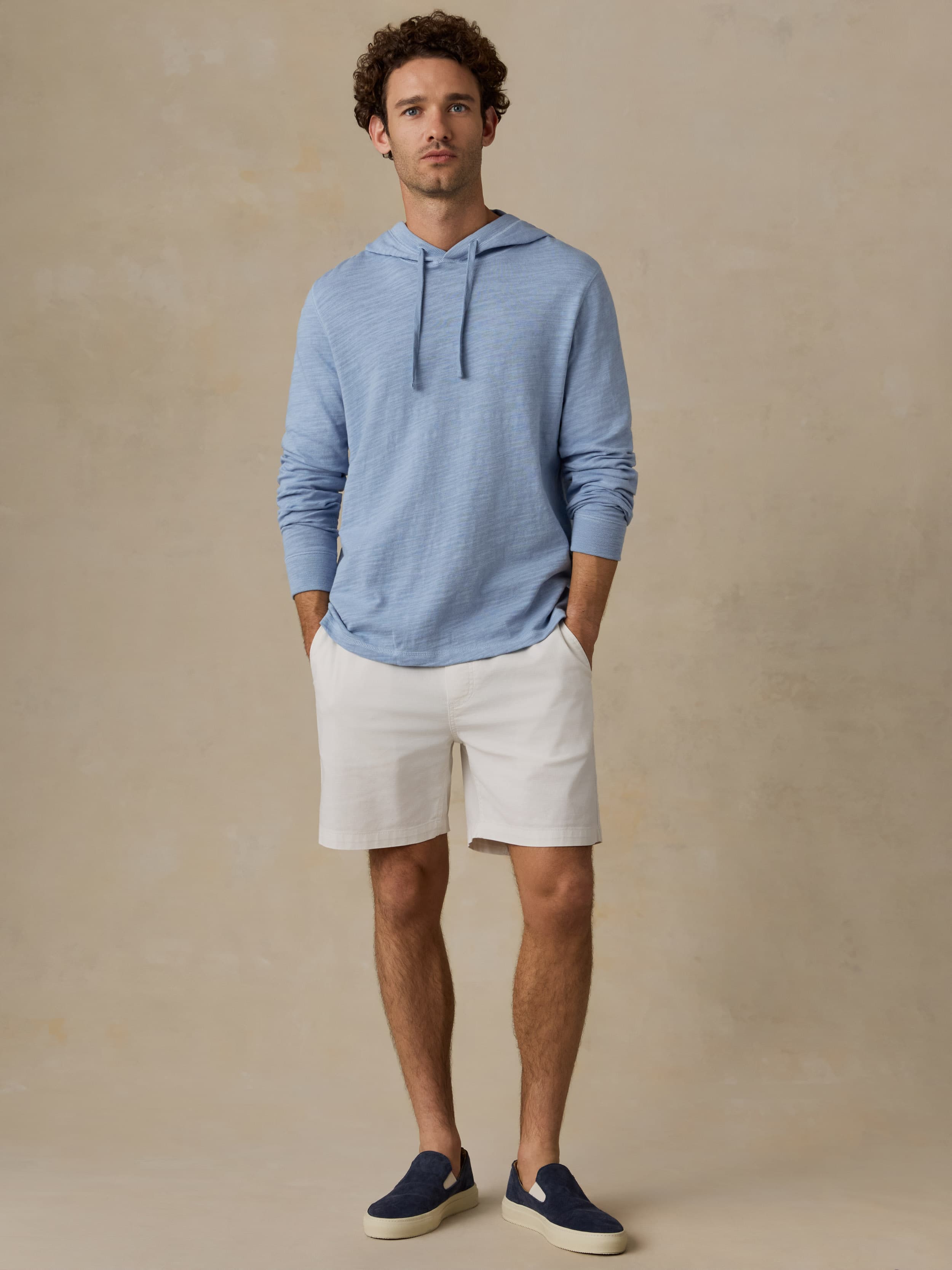 Man wearing a blue hoodie and beige shorts against a beige background