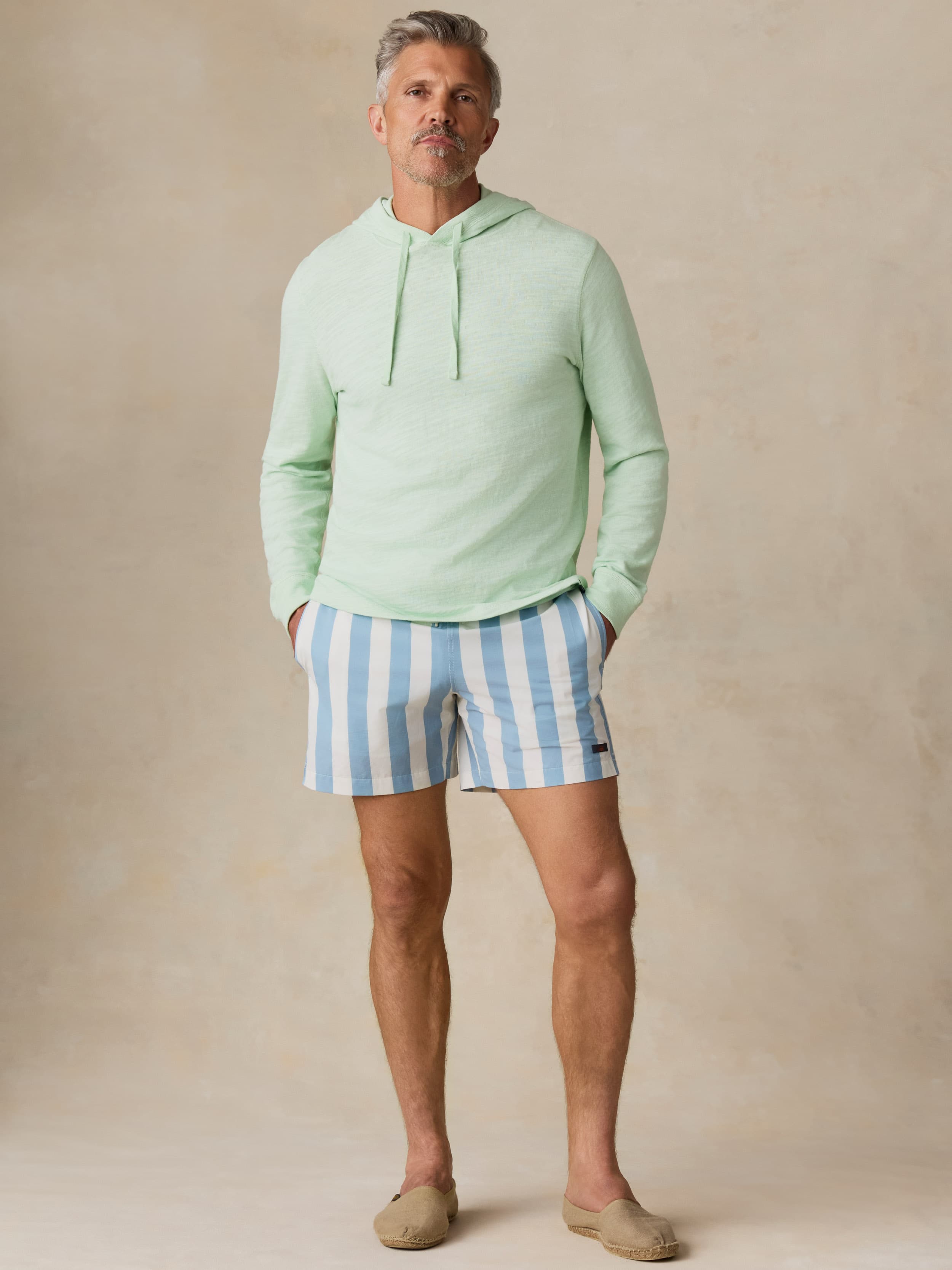 Man wearing a light green hoodie and blue striped shorts against a beige background