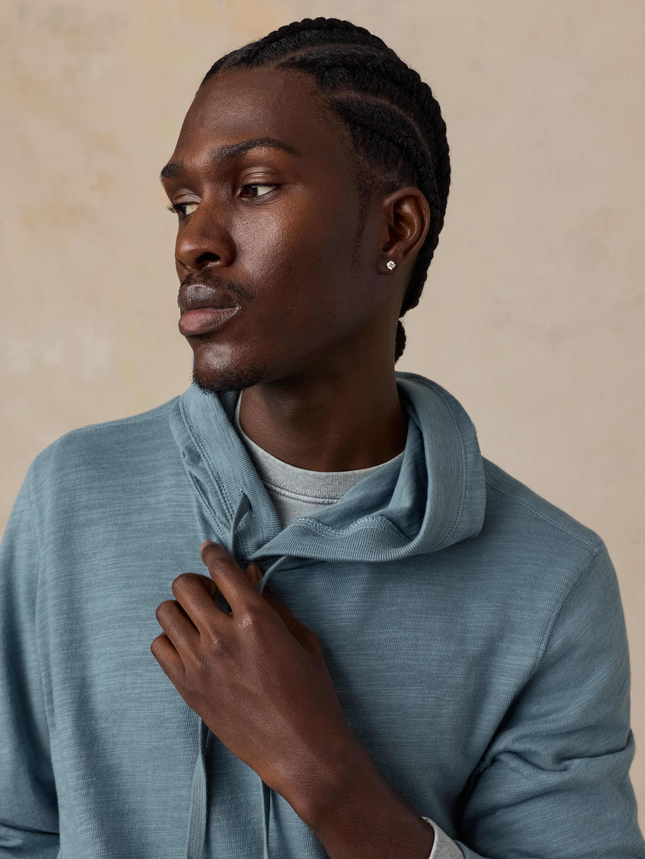 A man wearing a dusty blue-gray hooded knit sweatshirt over a light gray t-shirt.