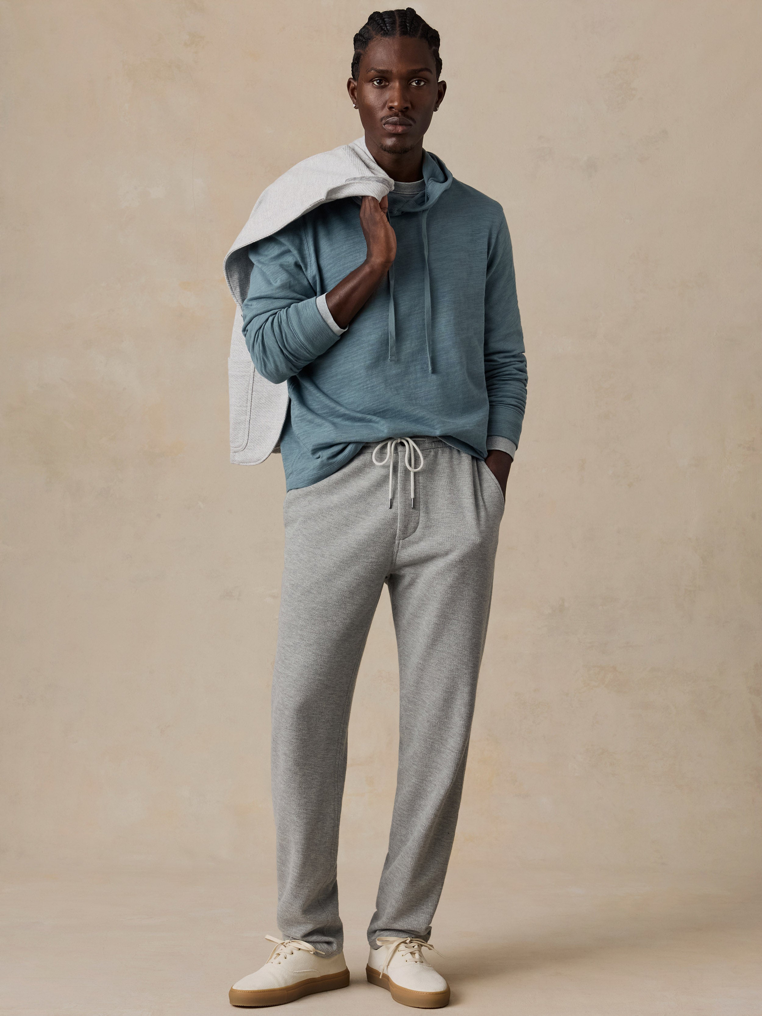 A model wearing a dusty blue long-sleeve hoodie, light gray drawstring sweatpants, and off-white sneakers.