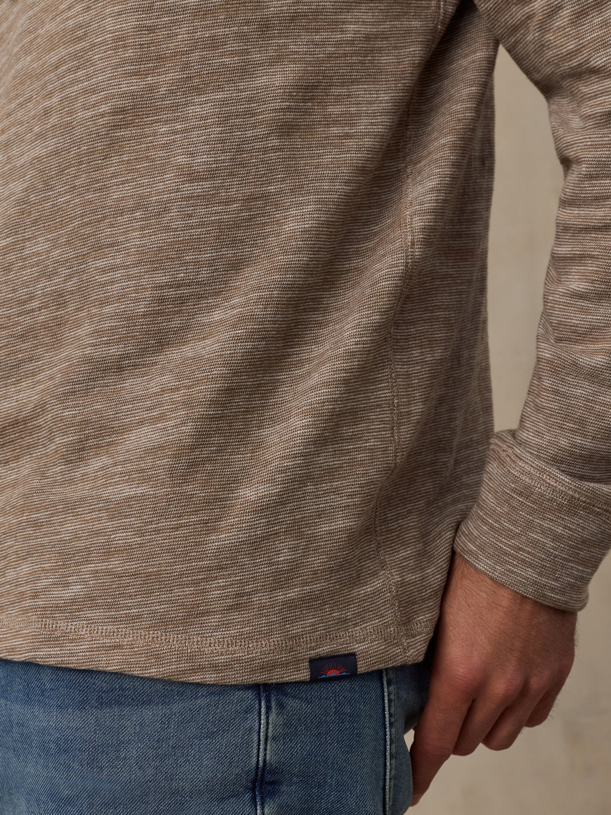 Close up of a man wearing a heathered taupe-brown long-sleeve hoodie and blue jeans, image 4 of 5