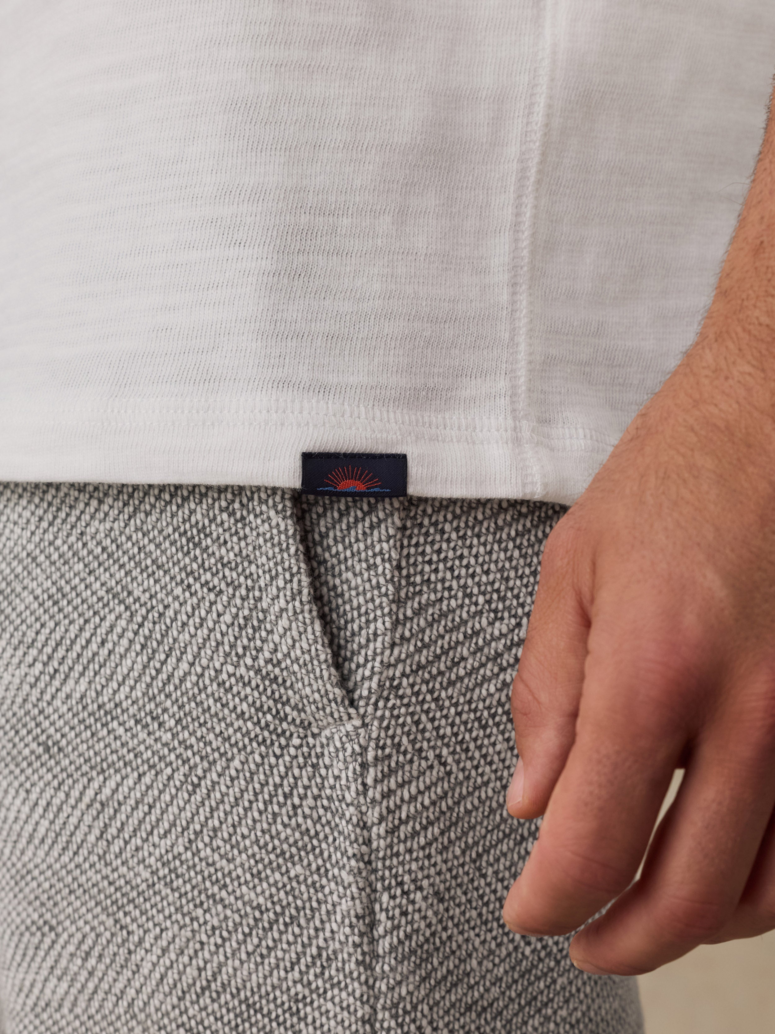 Close-up of a person wearing a white ribbed knit hoodie and textured gray herringbone sweatpants, with a small dark Faherty brand tab visible at the hem.