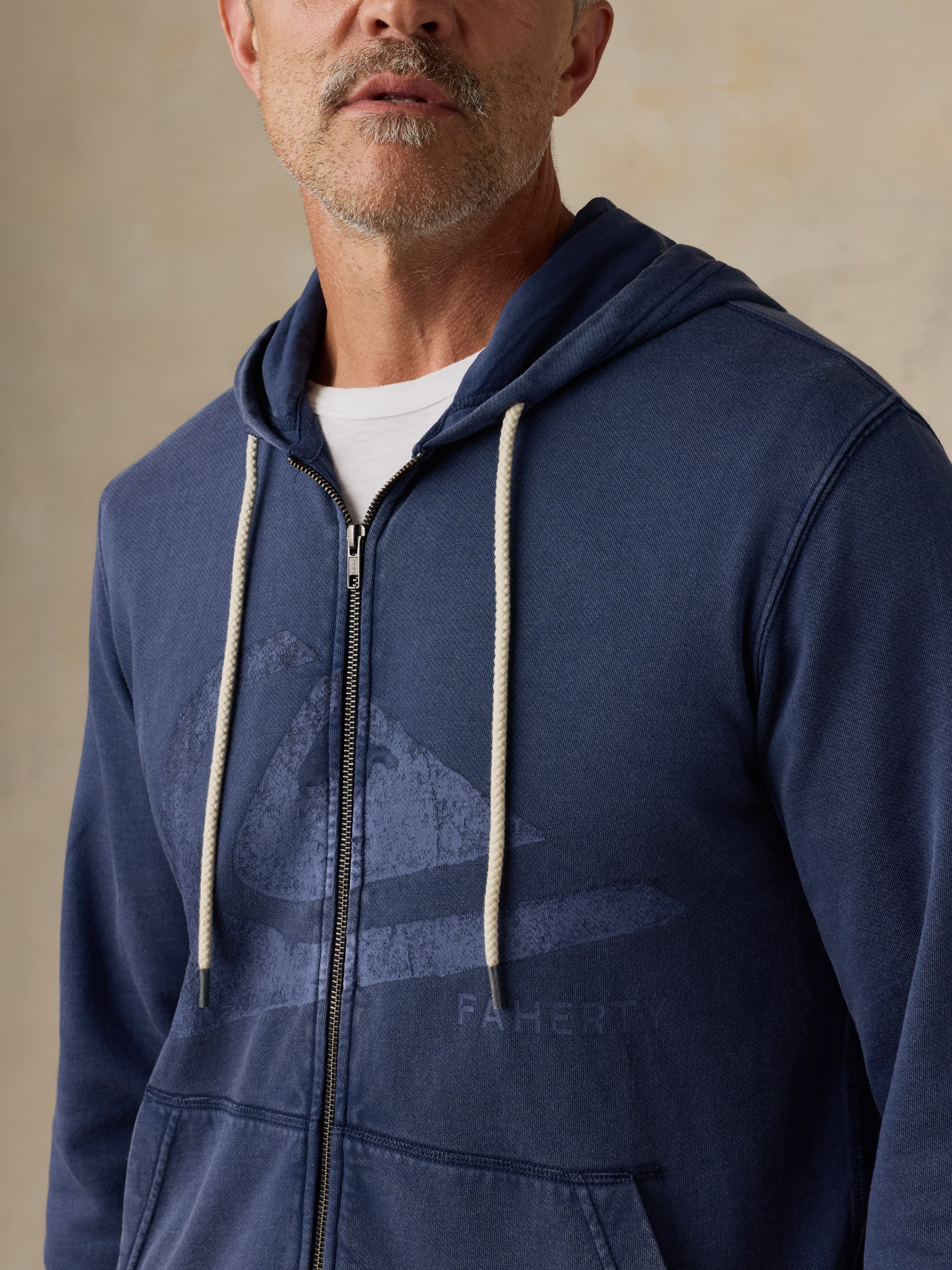 Man wearing a blue hoodie with a Faherty x Quiksilver logo on a beige background