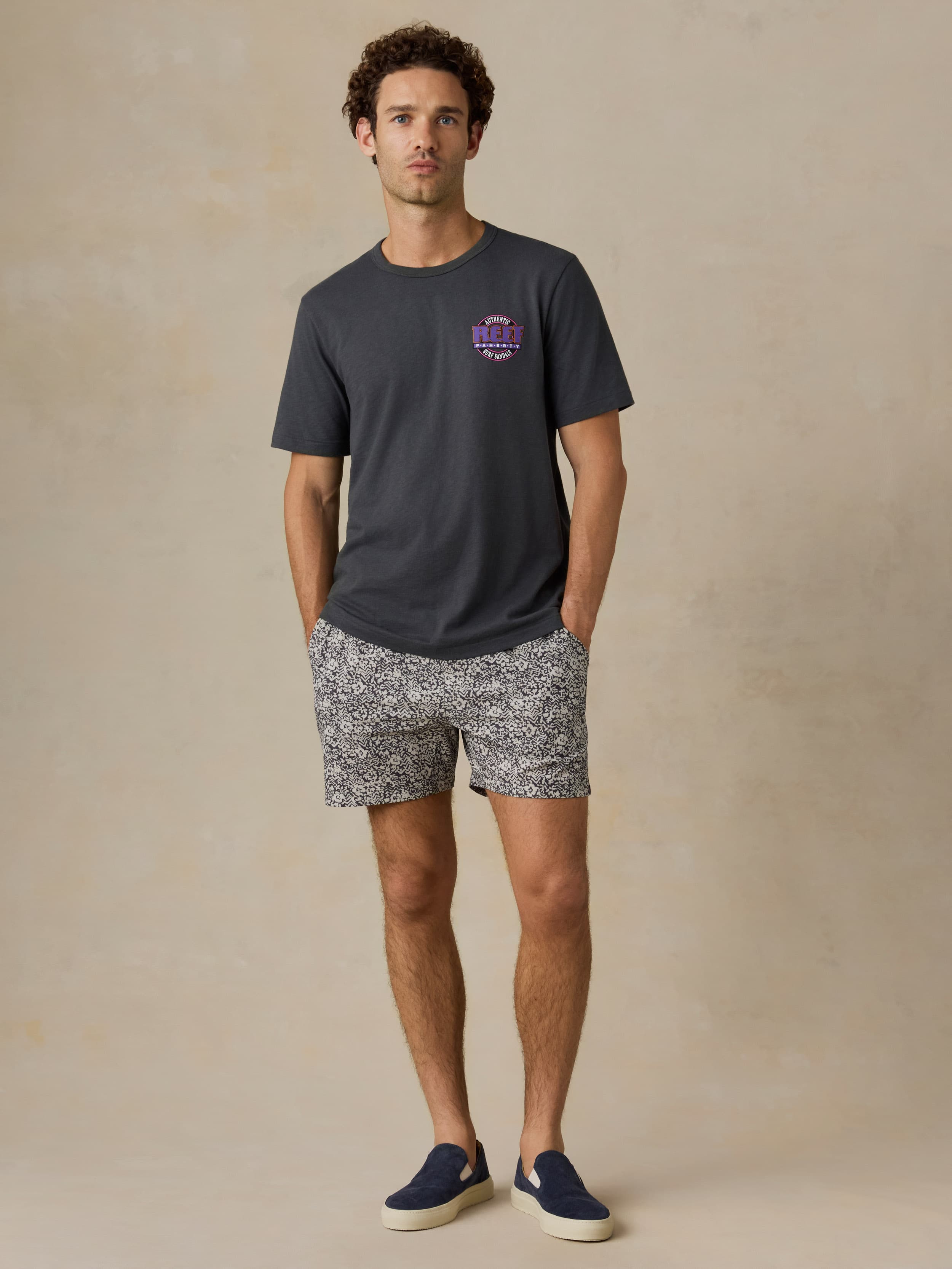 Man wearing a dark gray t-shirt and white and black patterned shorts on a beige background