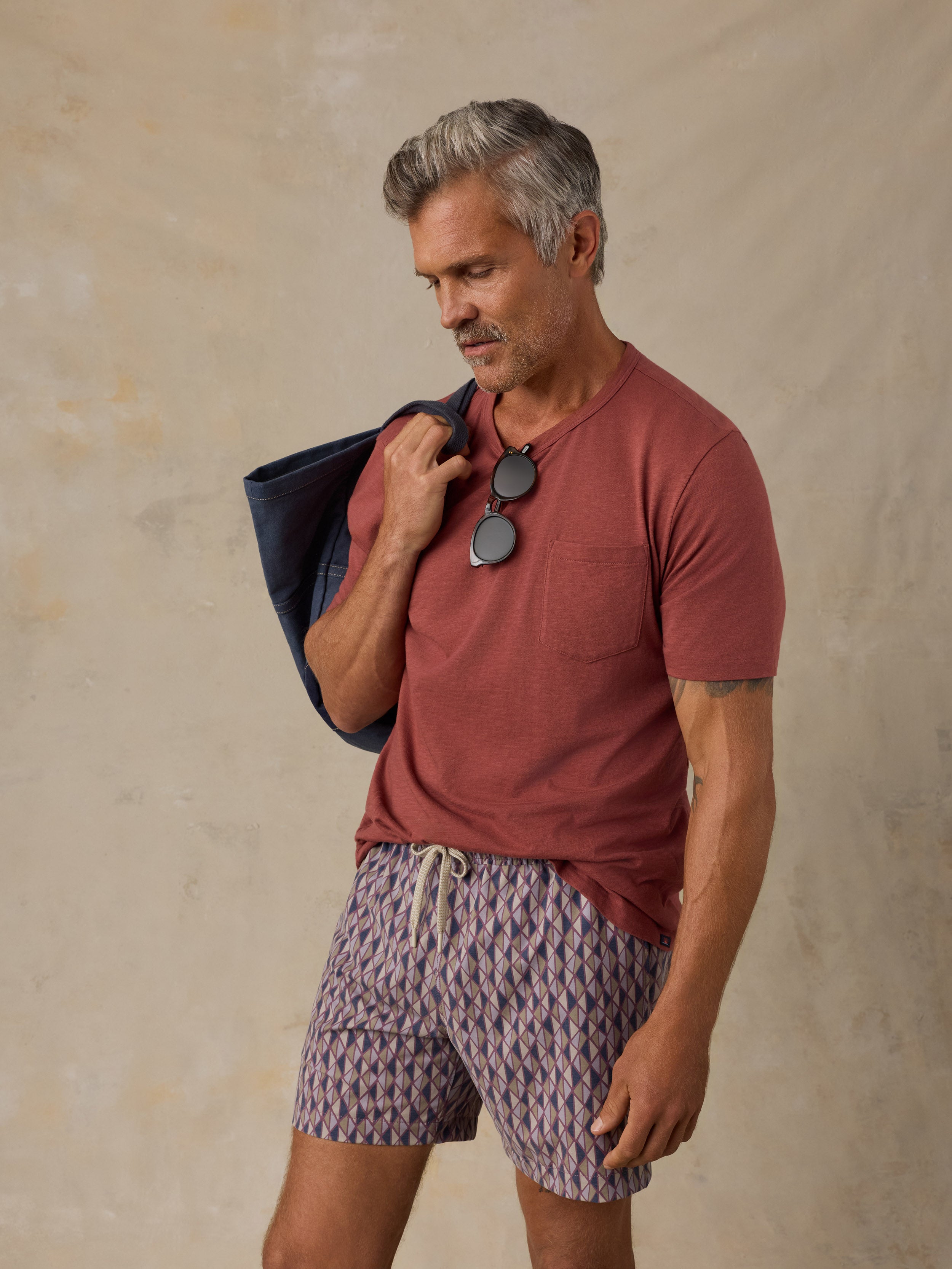 Man wearing a red t-shirt and purple geometric print swim shorts against a beige background