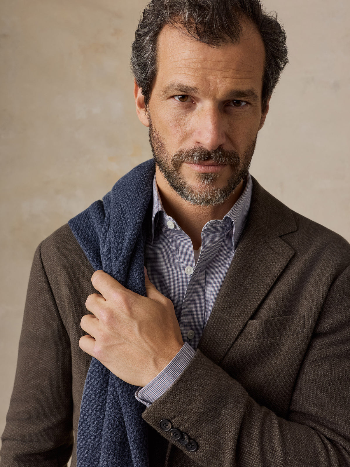 A man wearing a brown blazer and blue checkered shirt, image 4 of 5