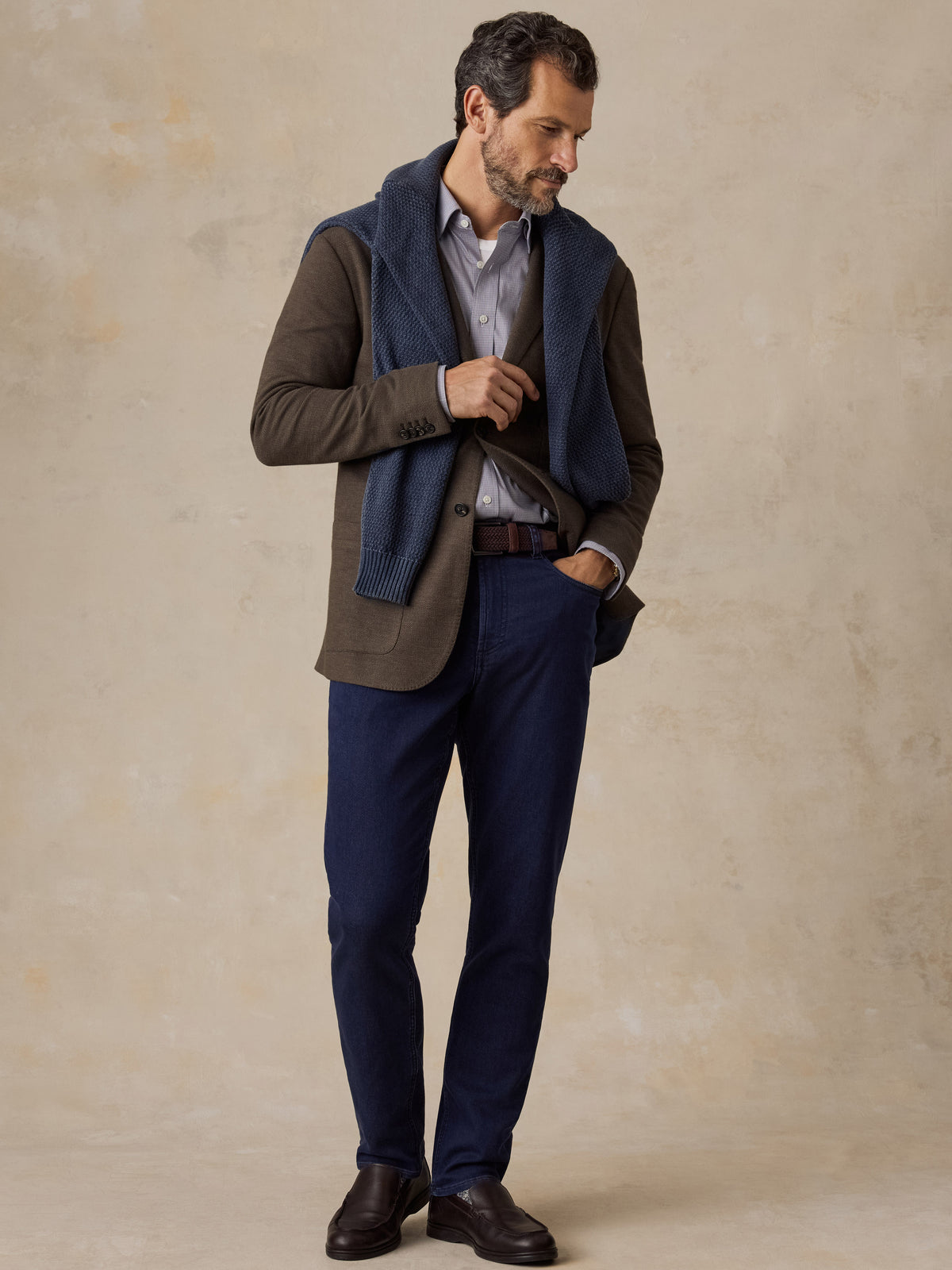 A man wearing a brown blazer with a blue shirt and blue jeans, image 5 of 5