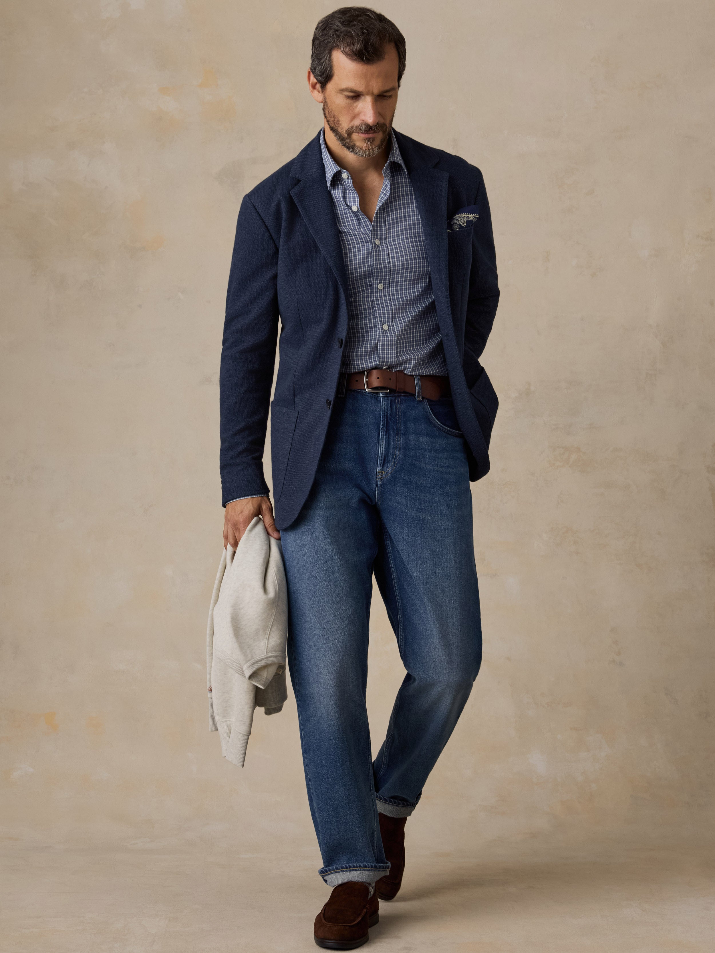 Man wearing a navy blazer over a blue button up shirt and blue jeans
