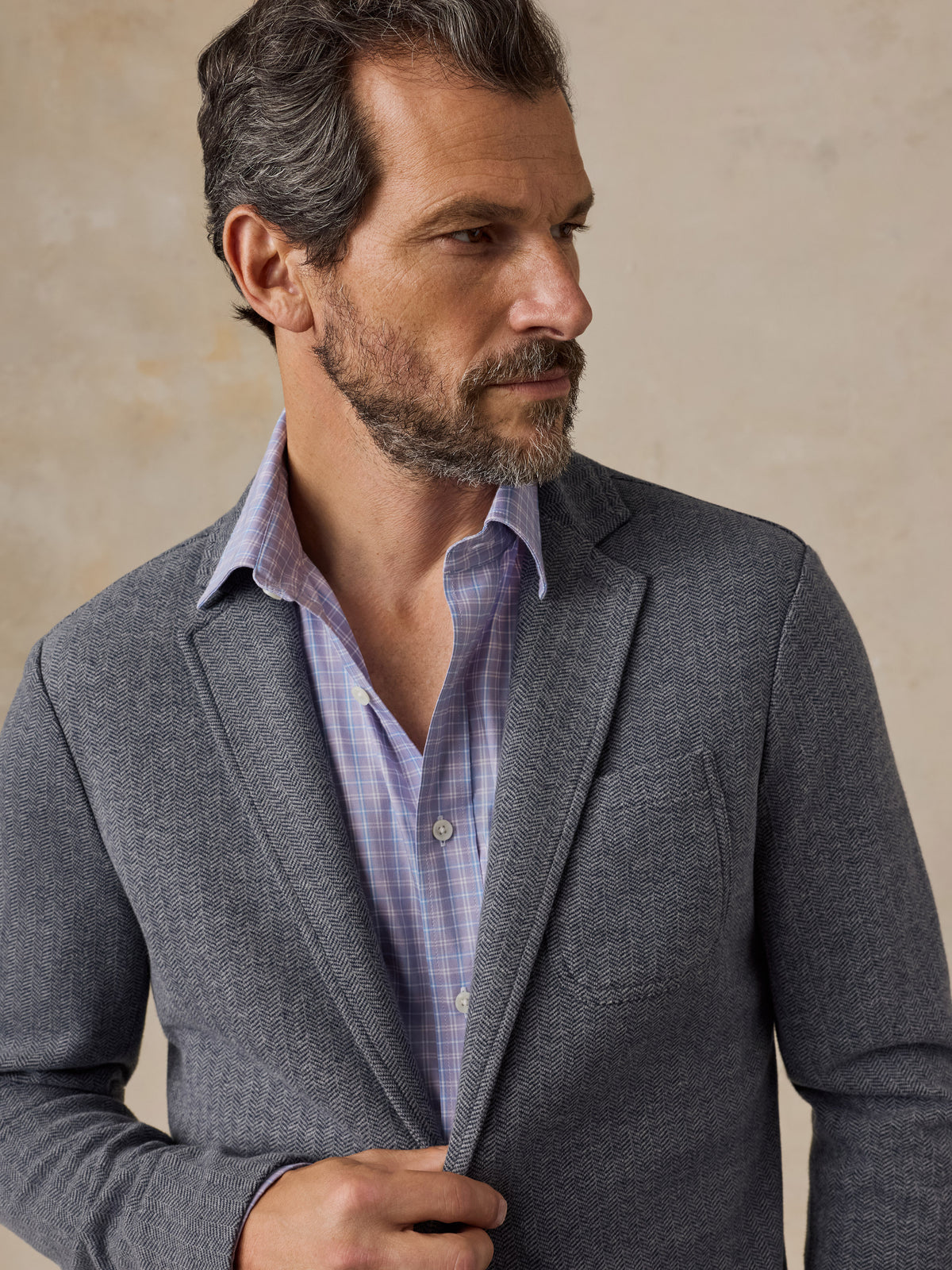 Close up of a man wearing a light purple plaid shirt and grey blazer, image 2 of 5