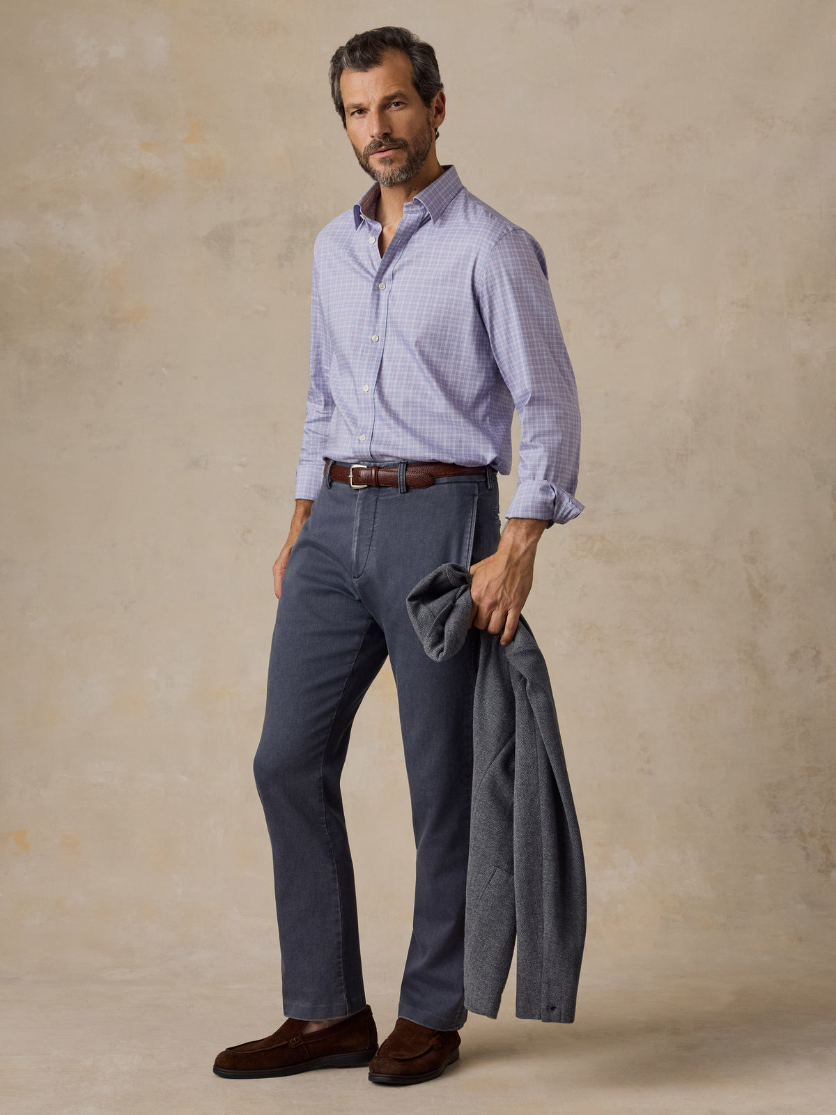 Man wearing a light purple plaid shirt, dark grey chino pants, and a grey blazer, image 5 of 5