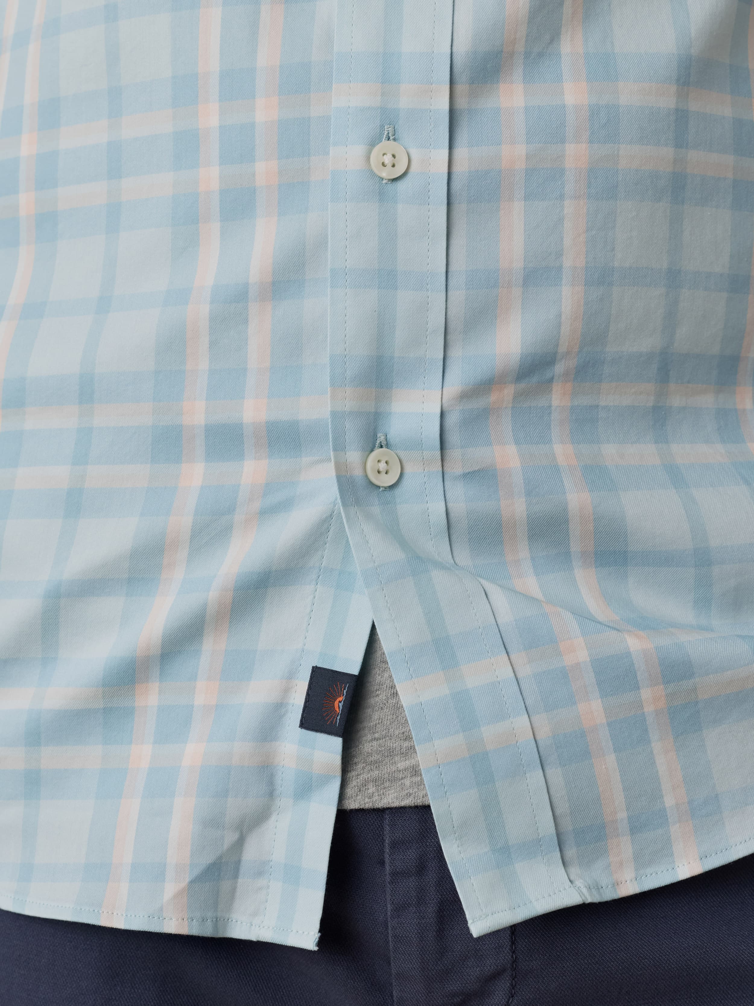 Close-up of a man wearing blue and white plaid shirt with Faherty brand logo near the hem