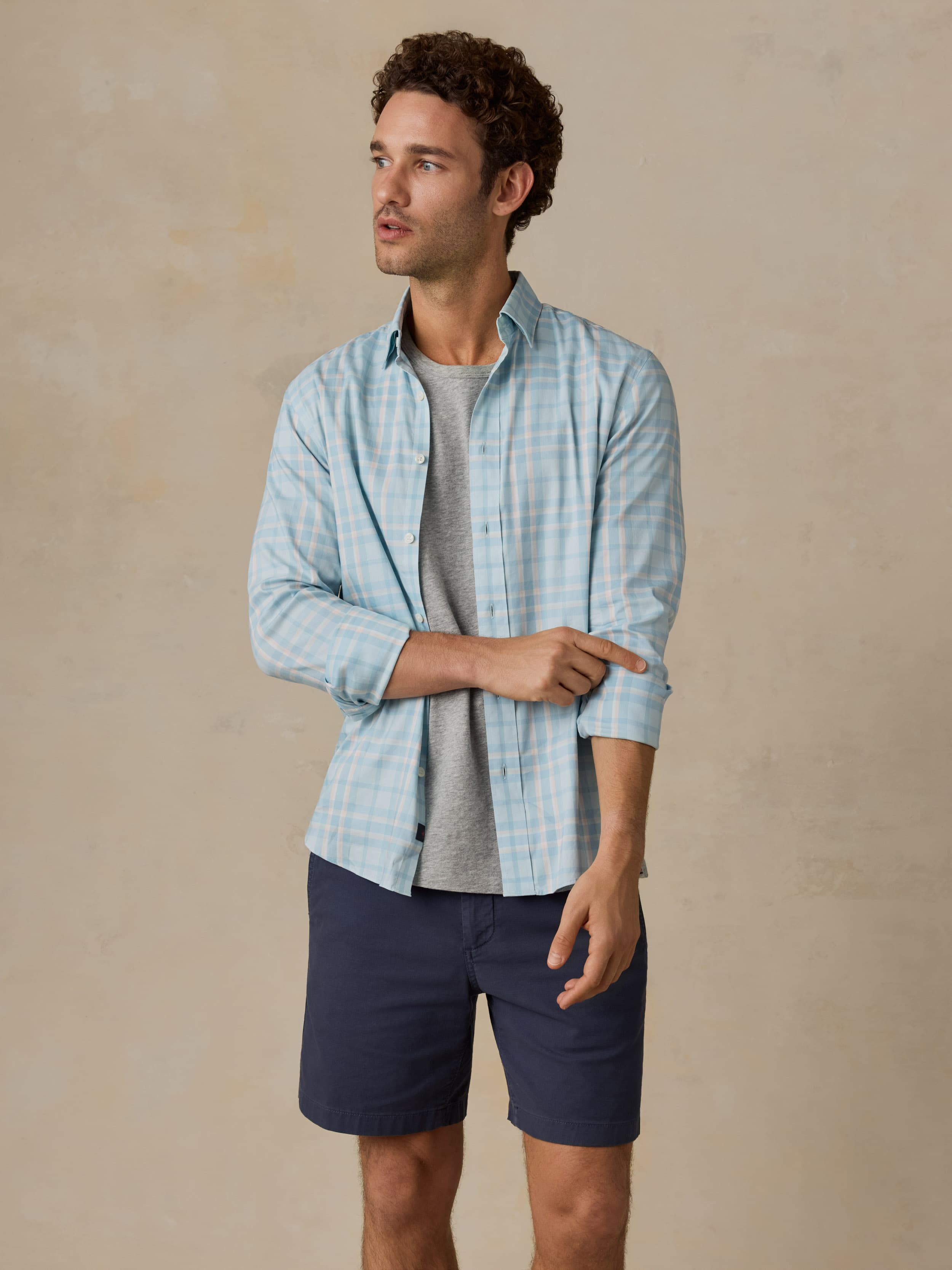 Man wearing blue and white plaid shirt with navy shorts against a beige background