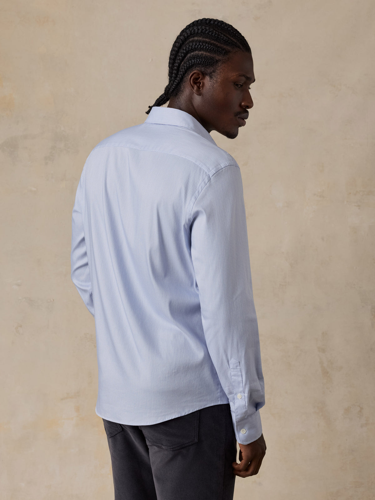 A man viewed from behind wearing a blue shirt and dark pants, image 2 of 5
