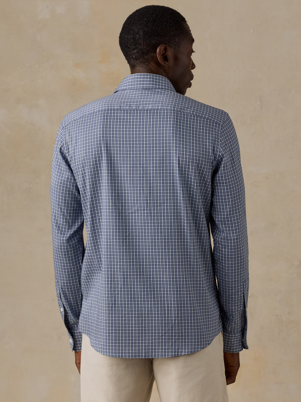 A man viewed from behind wearing a blue checkered shirt and beige shorts, image 3 of 5