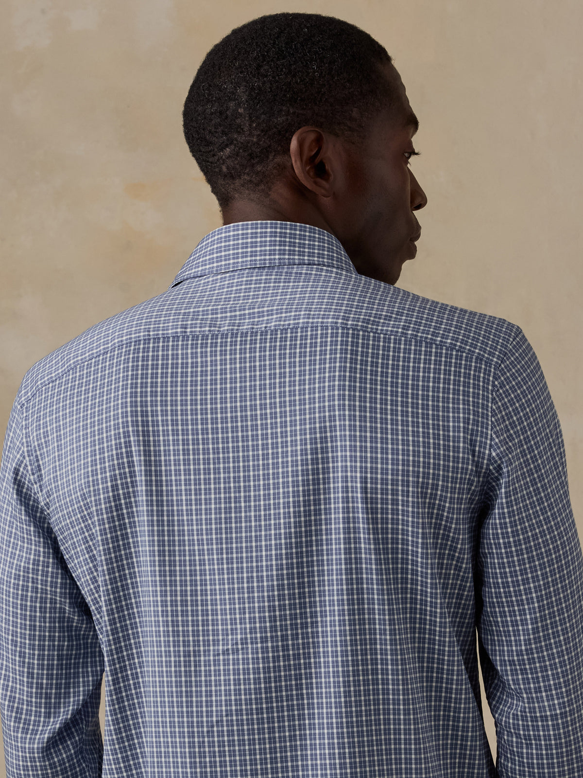 A man viewed from behind wearing a blue checkered shirt and beige shorts, image 4 of 5