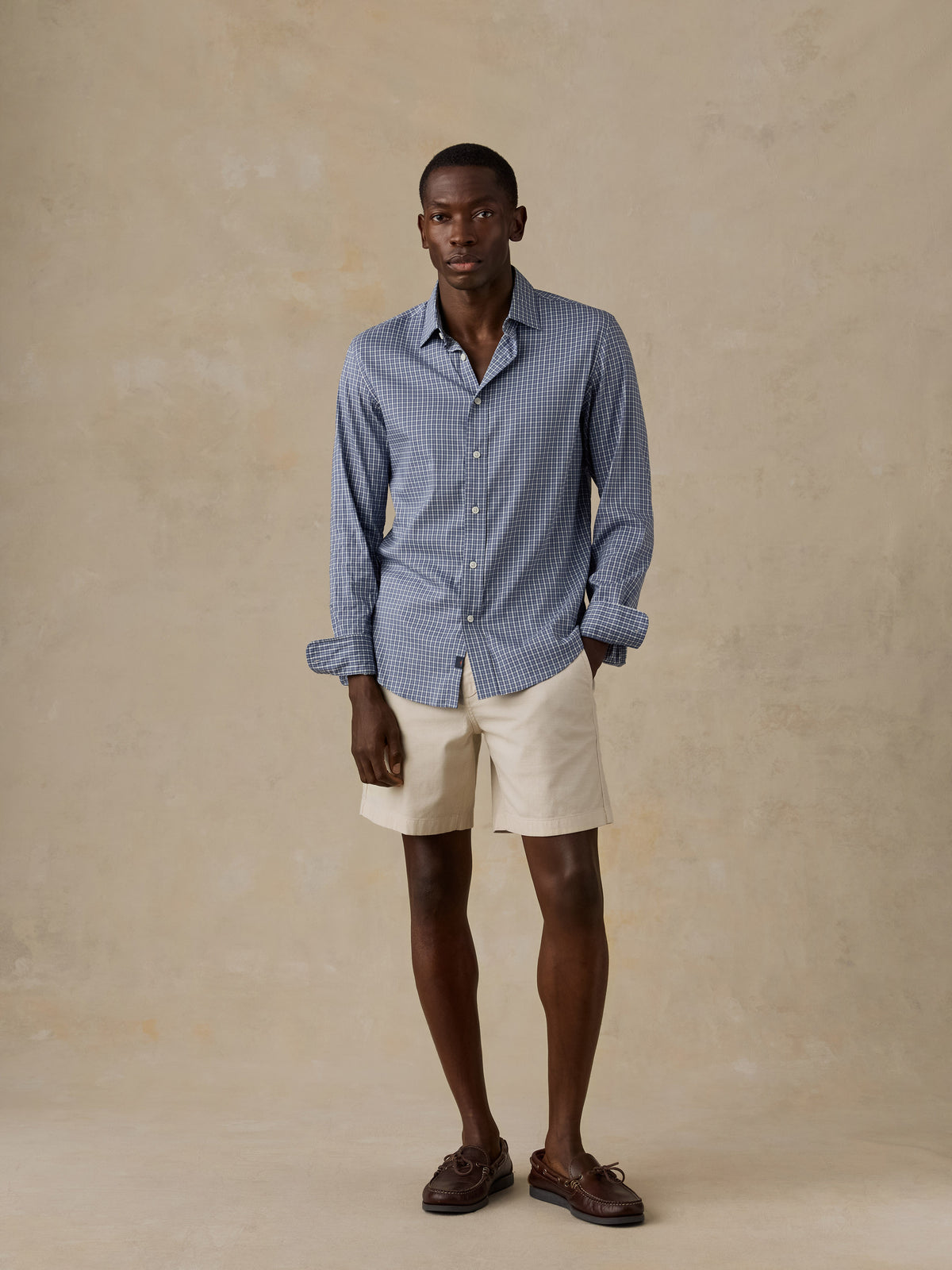 A man wearing a blue checkered shirt and beige shorts, image 5 of 5