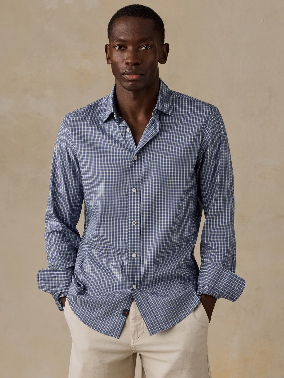 A man wearing a blue checkered shirt and beige shorts, image 1 of 5