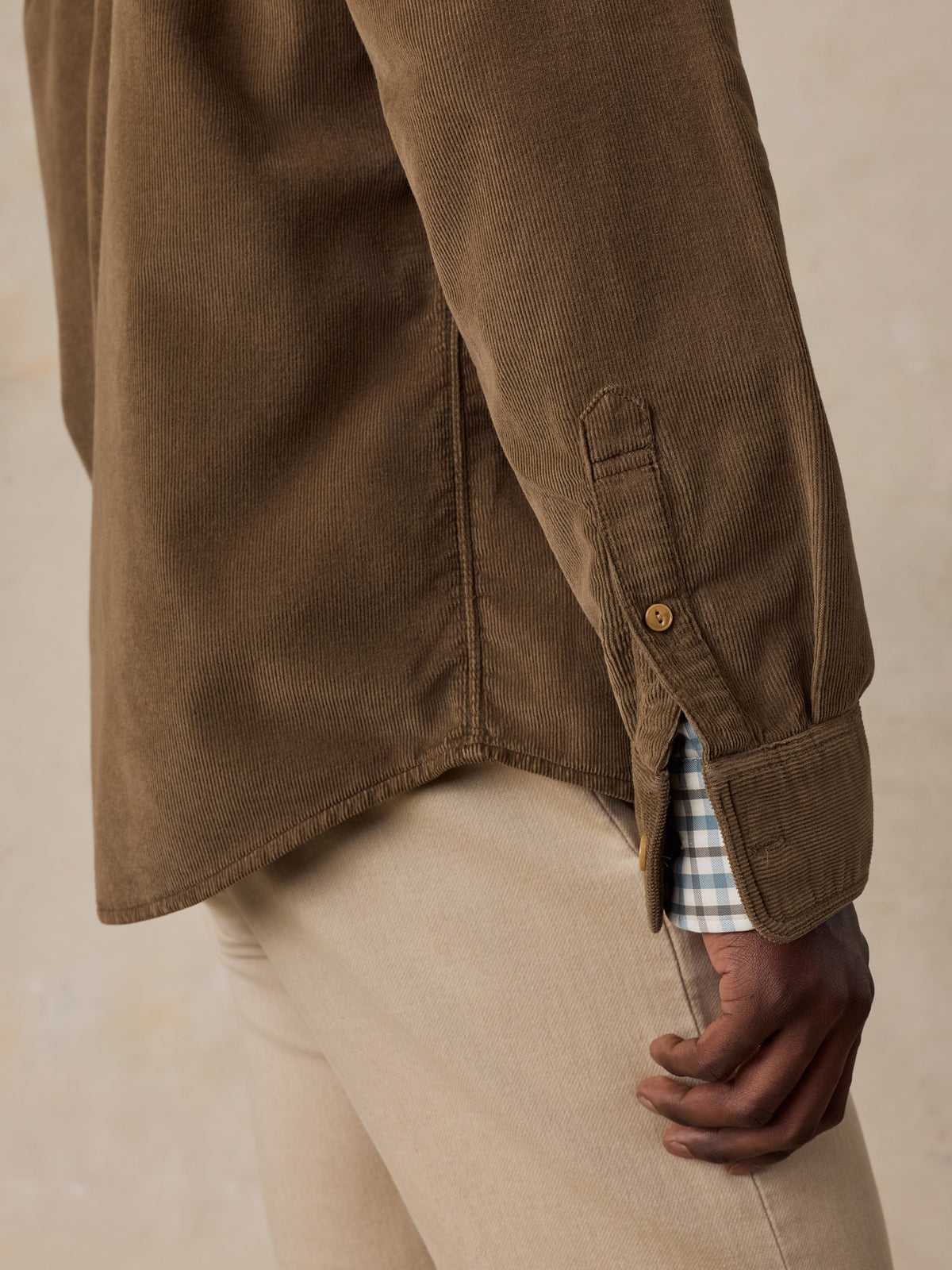 Close up of a man wearing a brown corduroy shirt over a plaid button down and beige pants, image 5 of 6