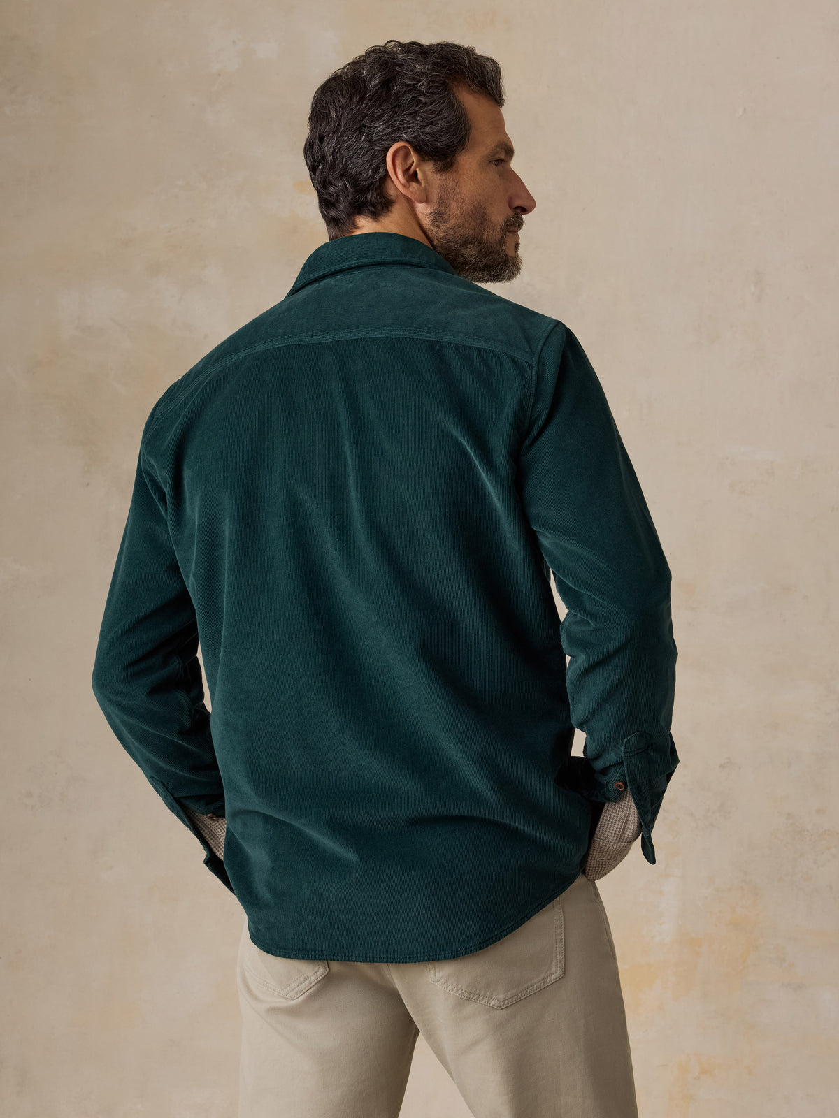 A man viewed from behind wearing a green overshirt and beige pants, image 2 of 5