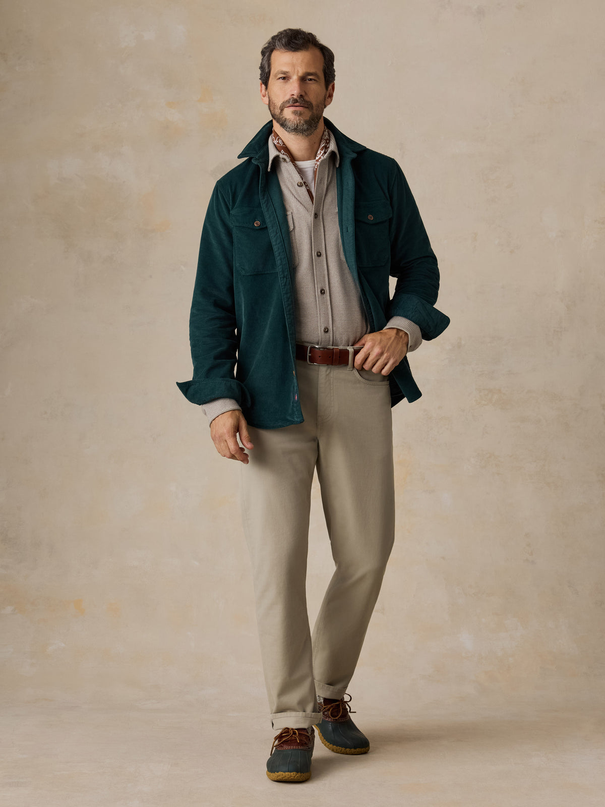 A man wearing a green overshirt, a beige check shirt, and beige pants, image 5 of 5