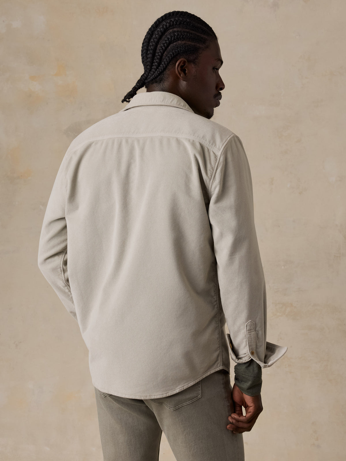 A man viewed from behind wearing a beige corduroy shirt and green pants, image 3 of 6