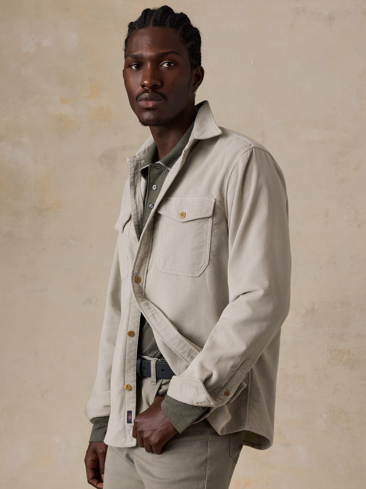 A man wearing a beige corduroy shirt over a green polo and green pants, image 5 of 6