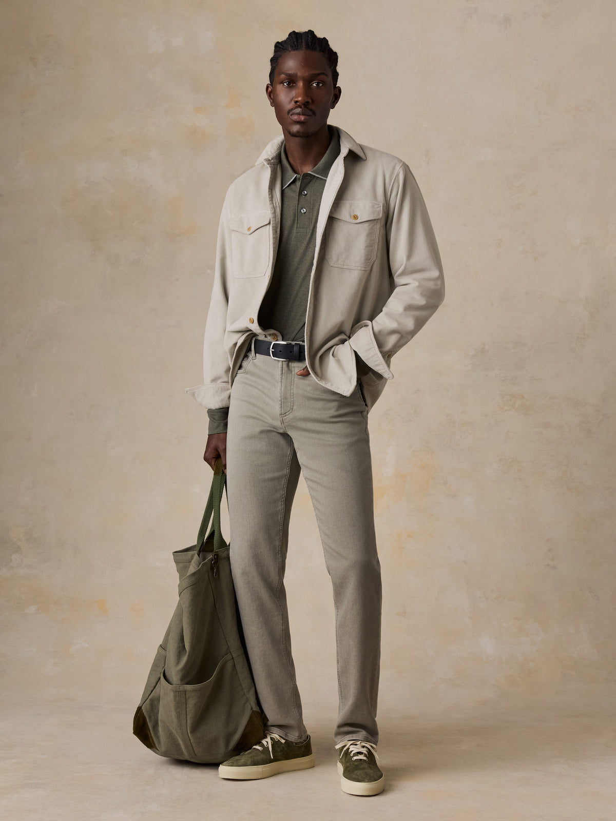 A man wearing a beige corduroy shirt over a green polo and green pants, holding a green tote, image 6 of 6