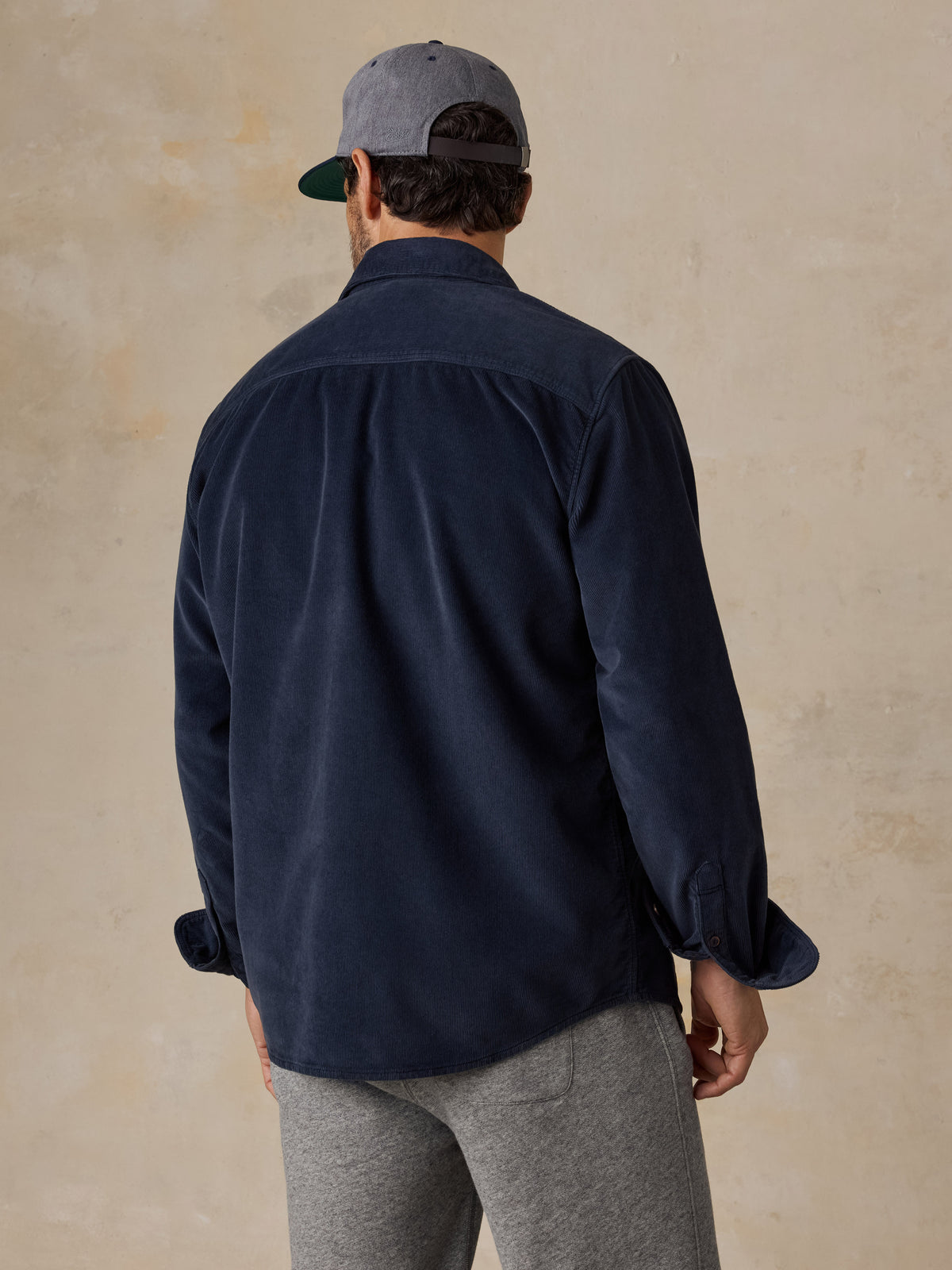 A man viewed from behind wearing a navy blue overshirt with grey sweatpants, image 3 of 6