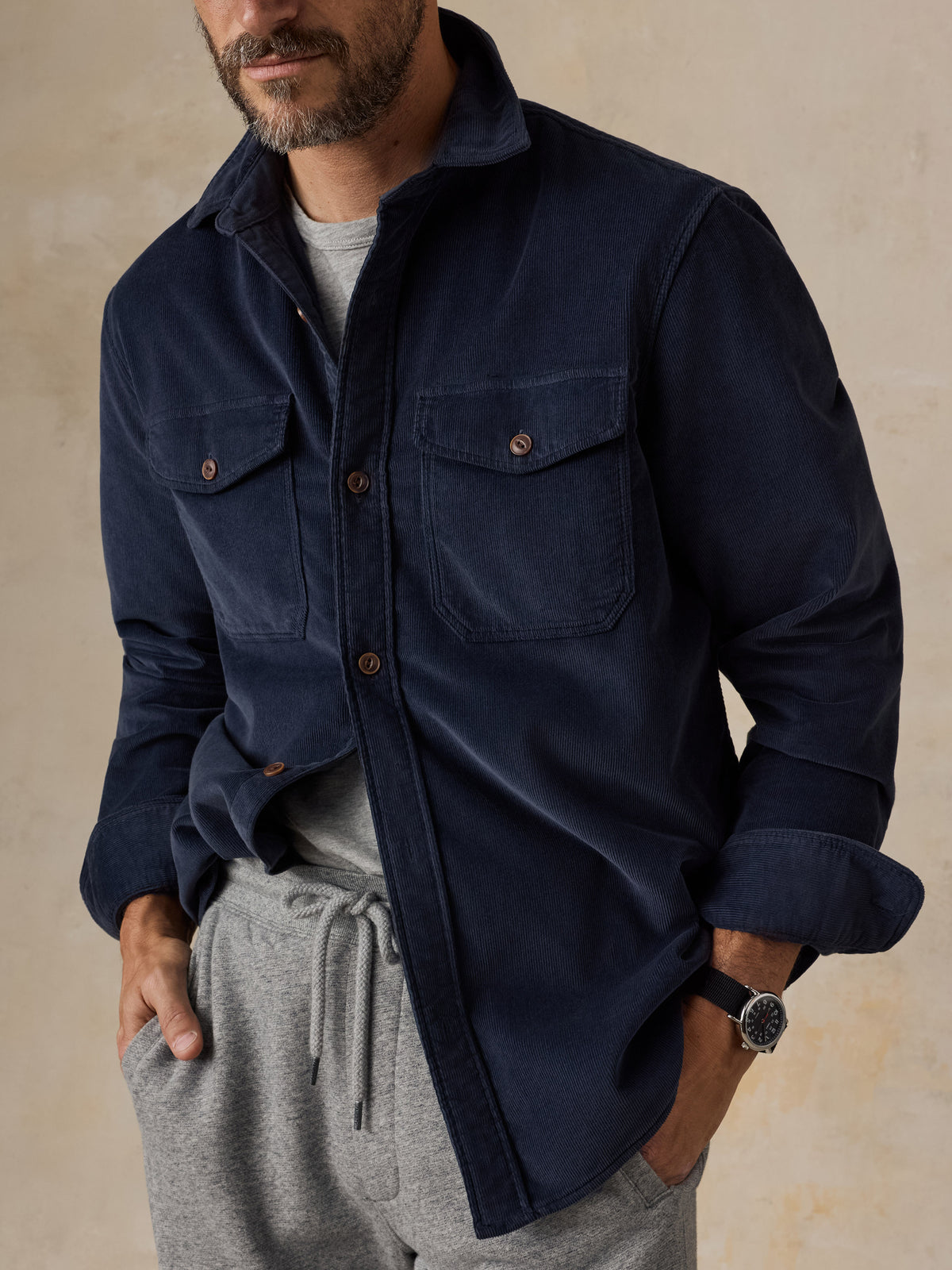 A man wearing a navy blue overshirt with a grey tee and sweatpants, image 4 of 6