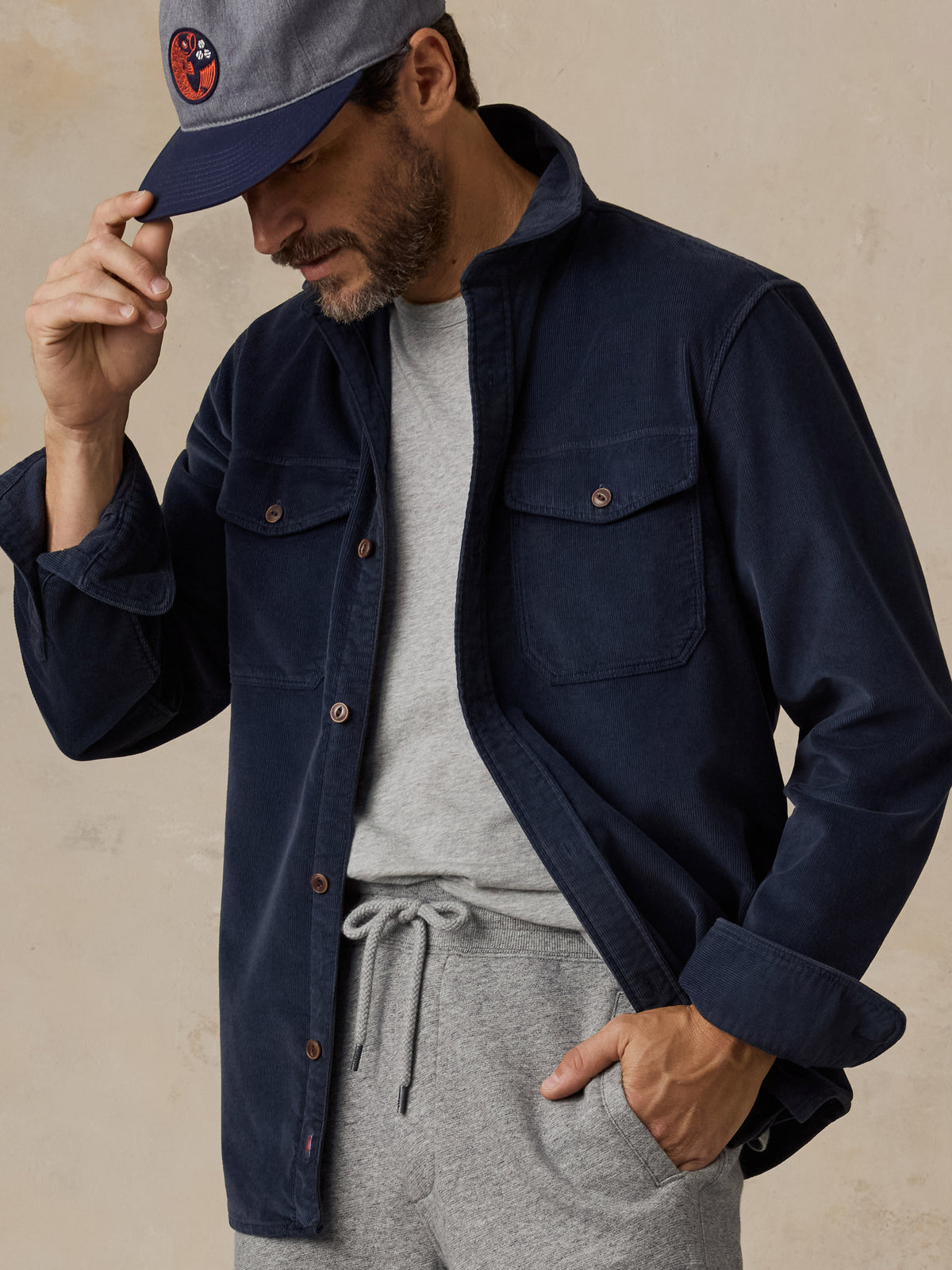 A man wearing a navy blue overshirt with a grey tee and sweatpants, image 5 of 6