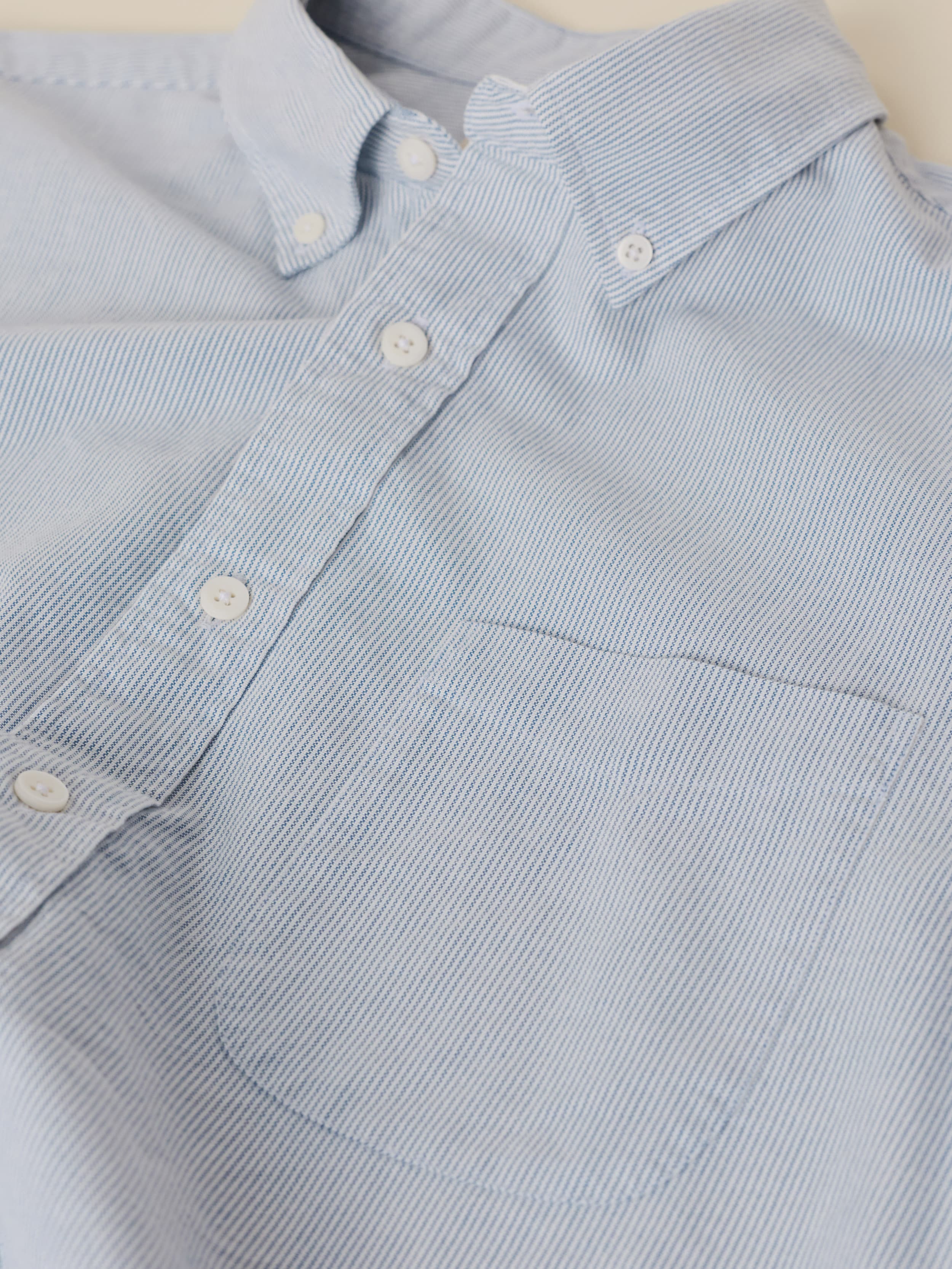 Close-up of a light blue striped shirt with buttons against a beige background
