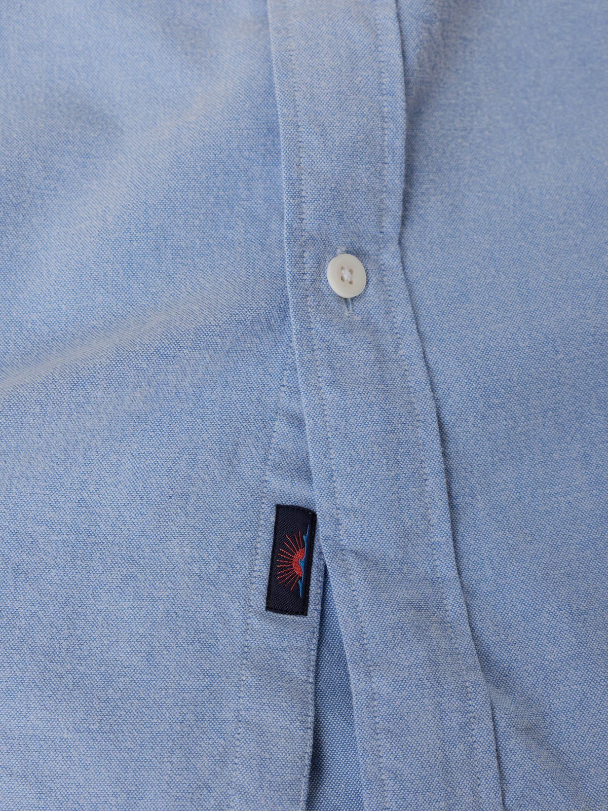 Close-up of a light blue button down shirt with a Faherty Brand sun and waves label near the hem, image 9 of 9