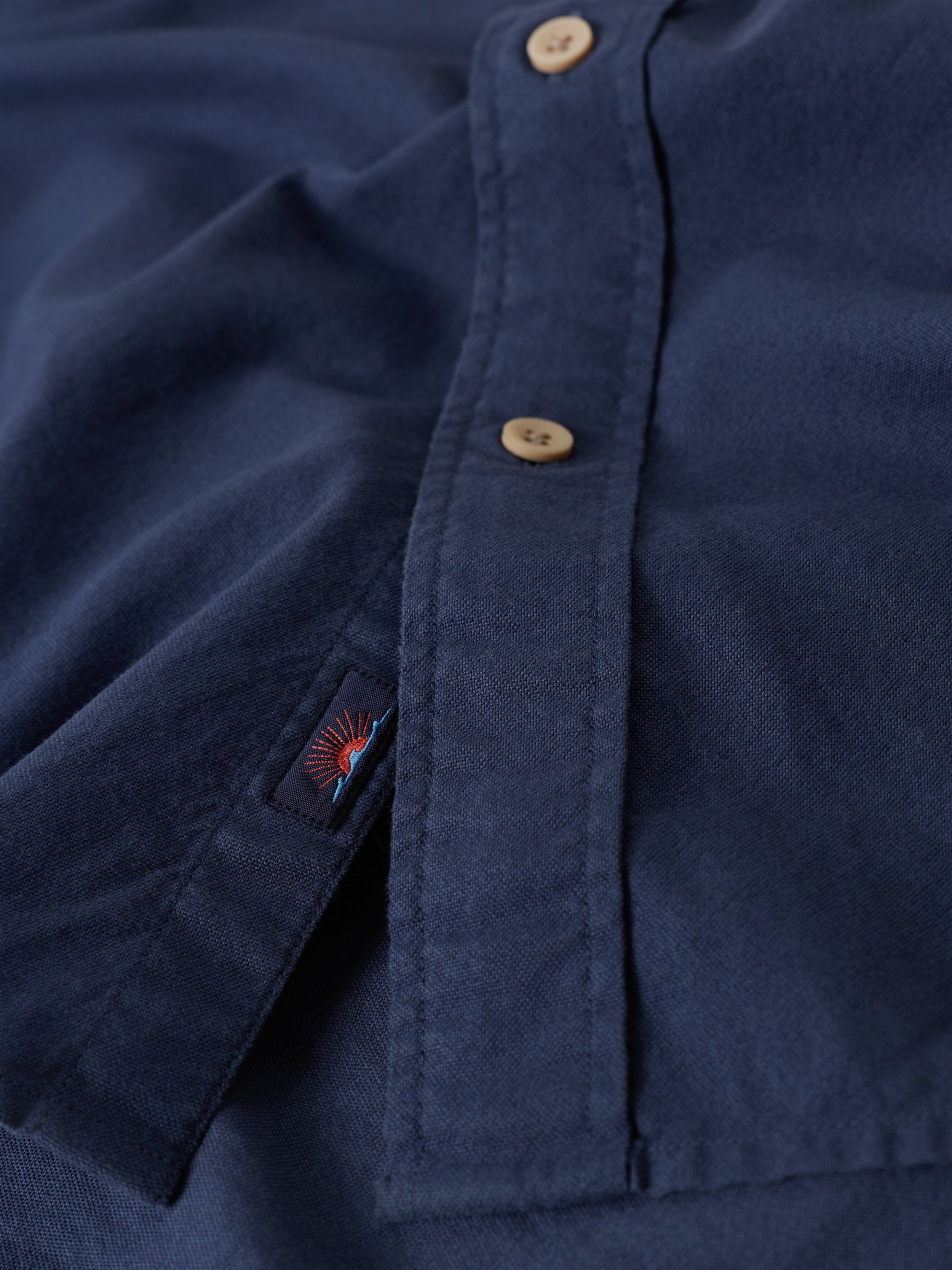 Close-up of a navy blue shirt with buttons and a Faherty brand logo on the placket.