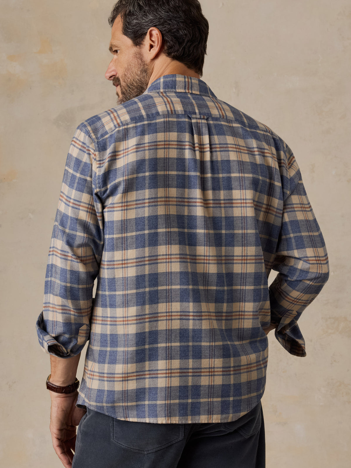 A man viewed from the back wearing a blue and beige plaid shirt and dark pants, image 2 of 5
