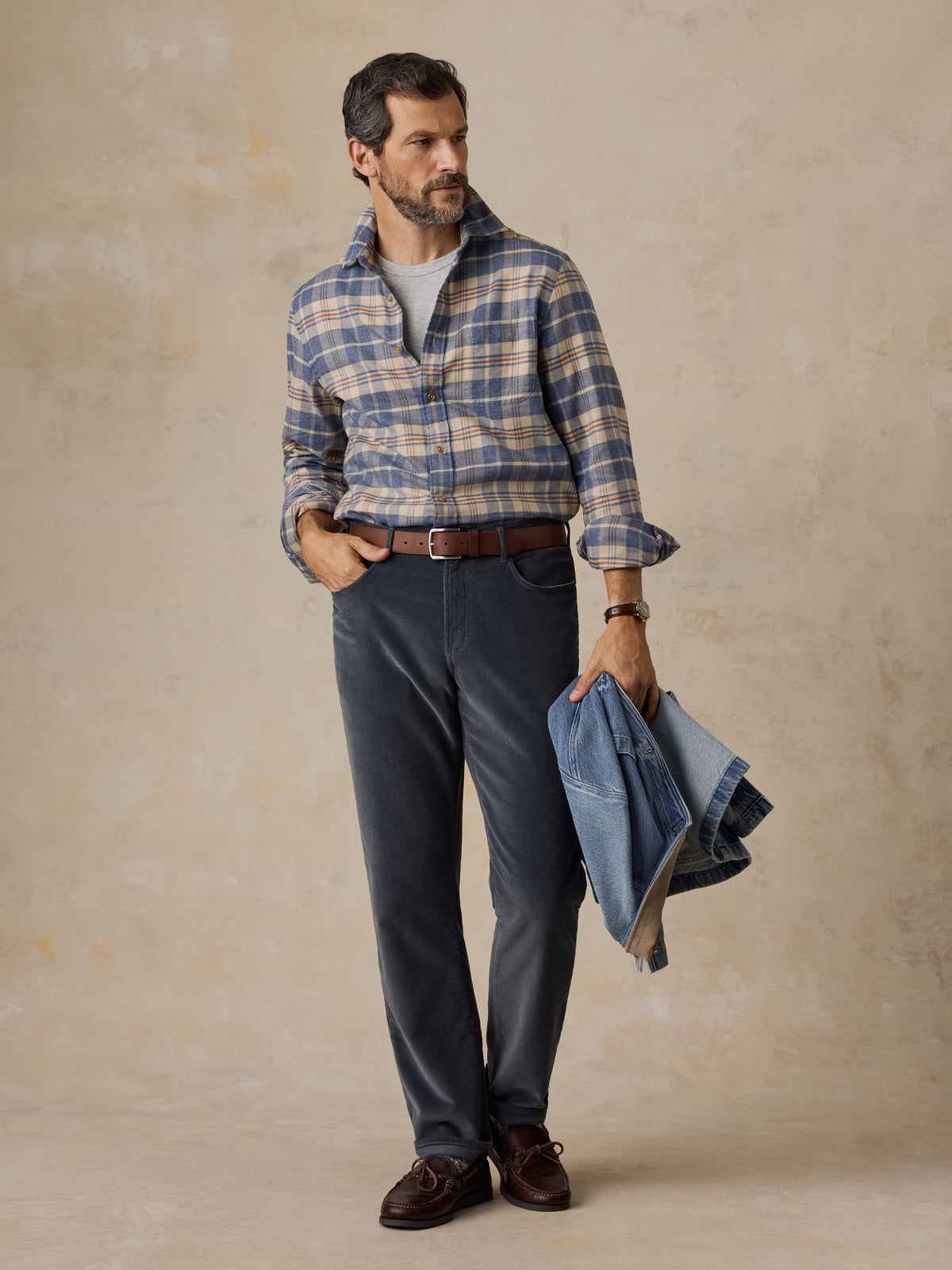 A man wearing a blue and beige plaid shirt and dark pants, image 5 of 5