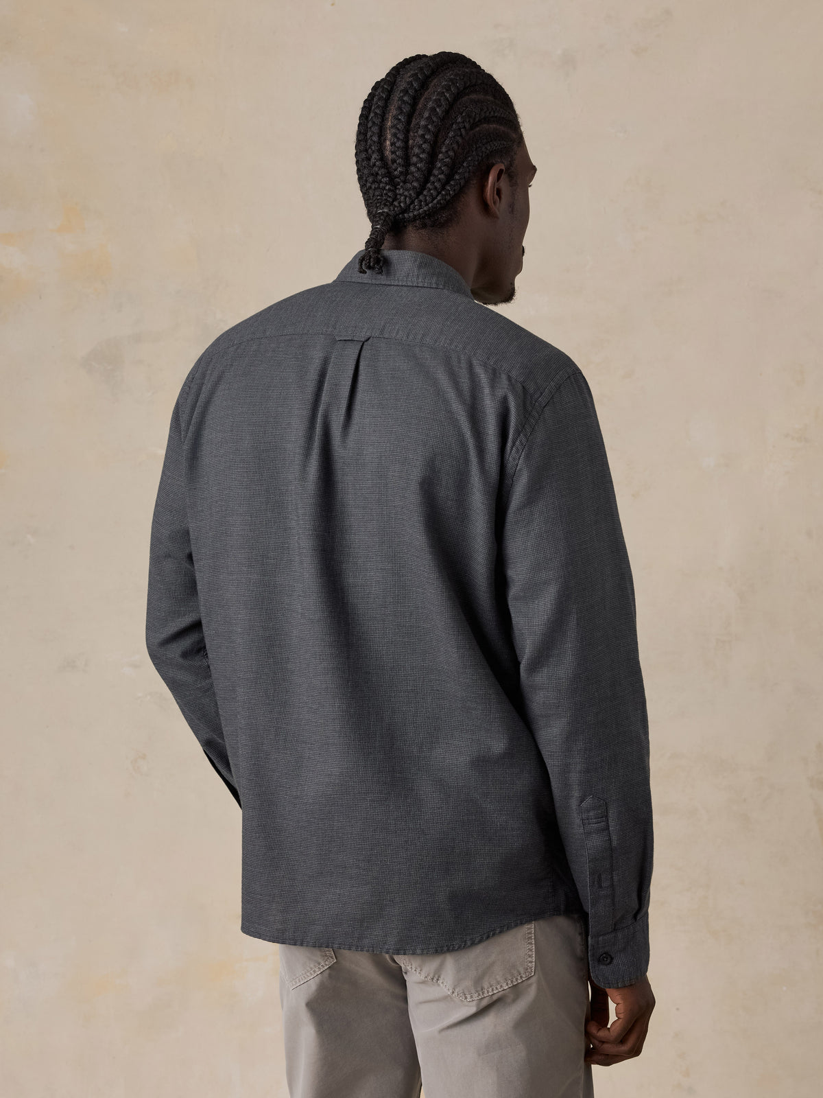 A man viewed from behind wearing a dark grey button down shirt and grey pants, image 2 of 5