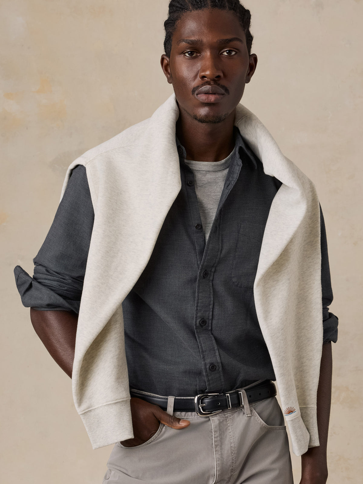 A man wearing a dark grey button down shirt with grey pants and a crewneck, image 4 of 5