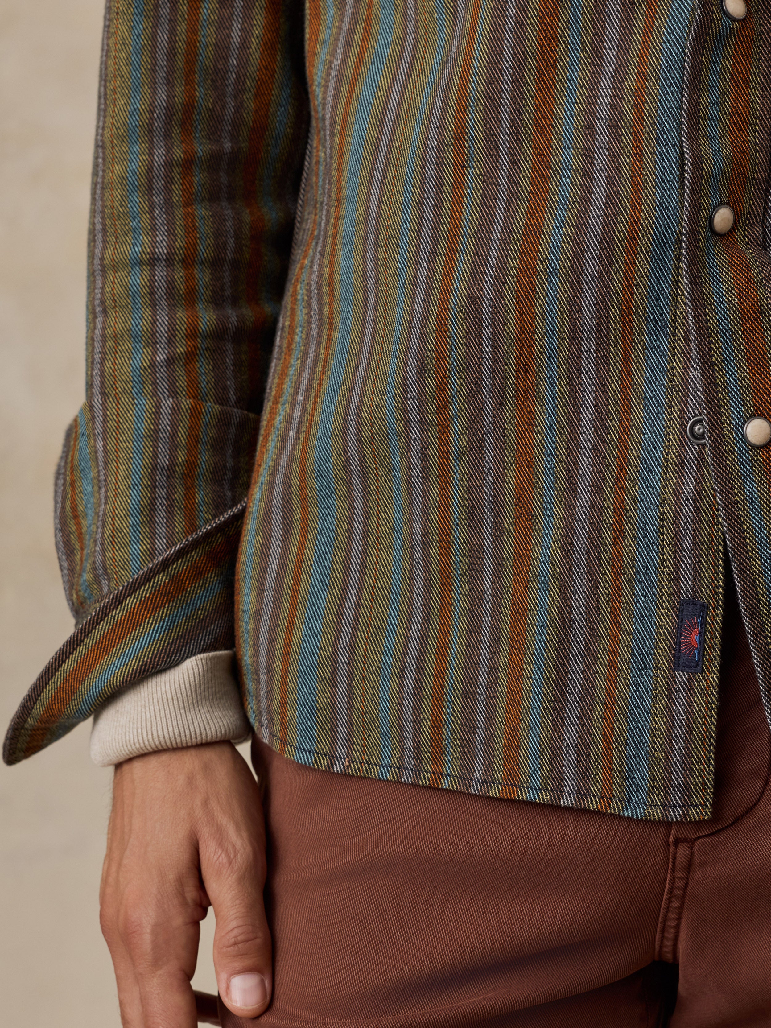 Close up of a man wearing a colorful western shirt with white snap buttons and a small Faherty brand tag near the hem