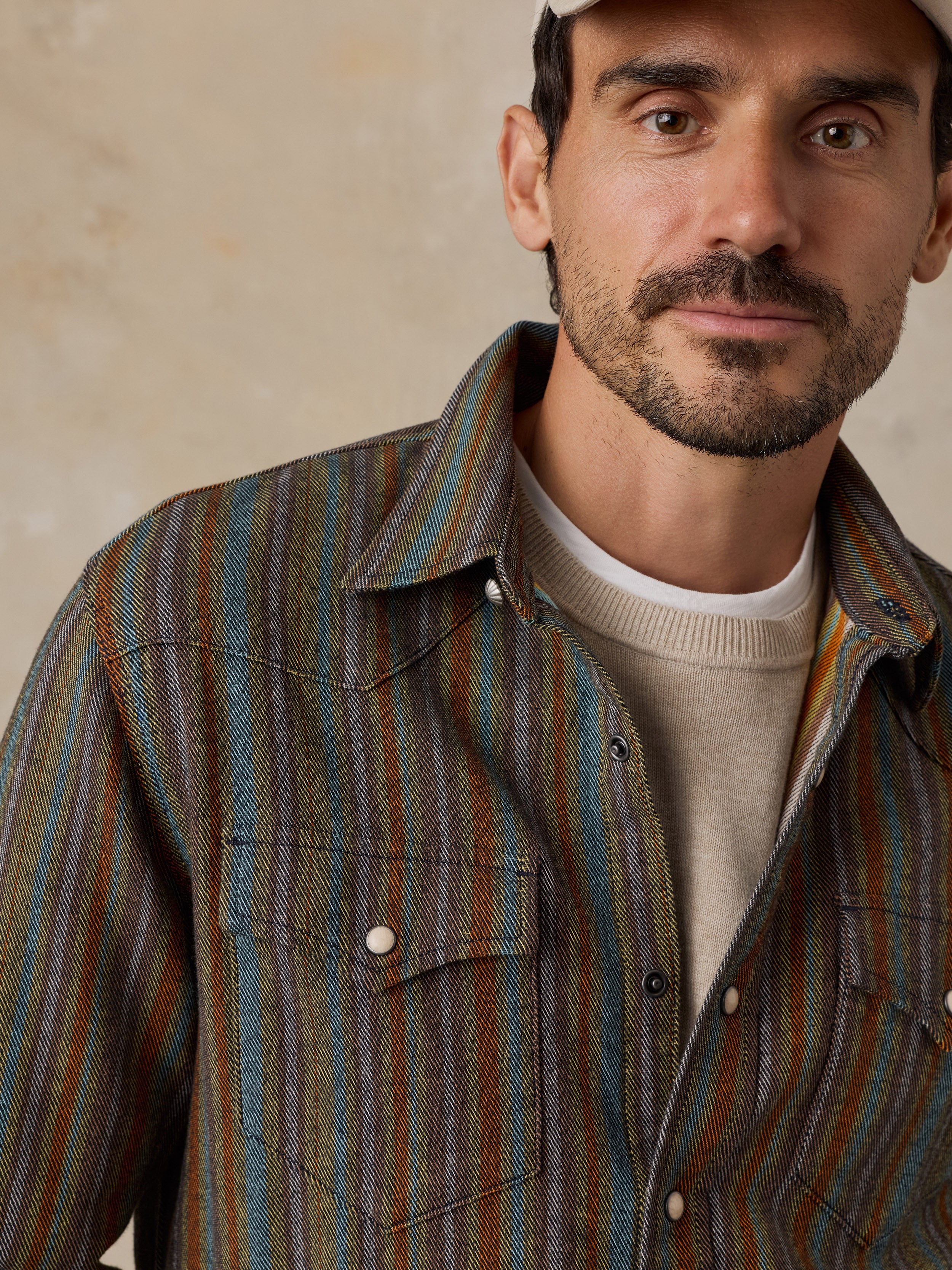 A man wearing a striped button-down shirt with blue, green, and brown vertical stripes