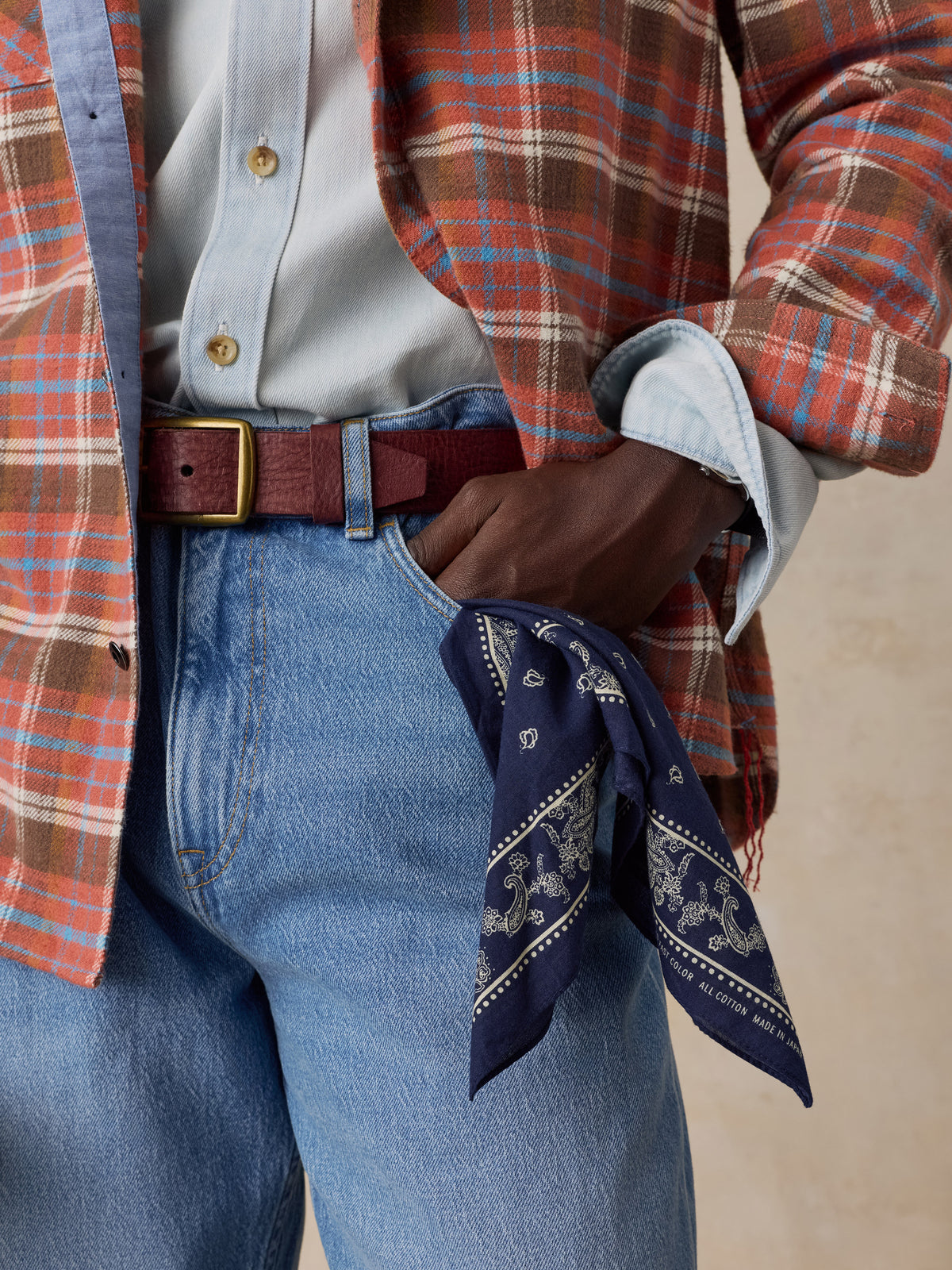 Close up of a man wearing a red plaid flannel over a chambray shirt and blue jeans, image 5 of 5