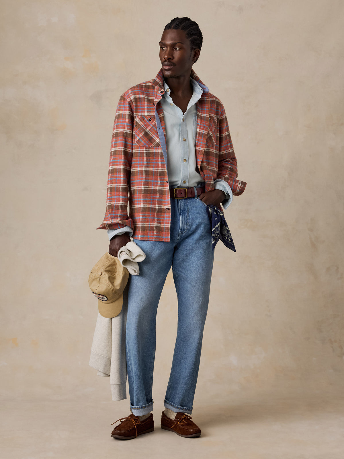 A man wearing a red plaid flannel with a chambray shirt, blue jeans, and brown loafers, image 2 of 5