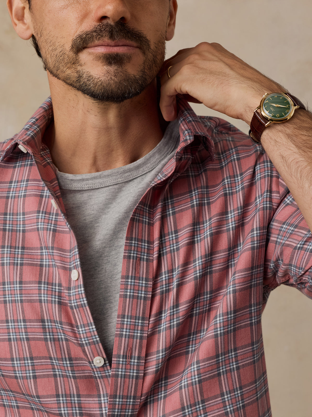 A close-up lifestyle shot of a man wearing a red and navy plaid button-down shirt over a gray t-shirt.